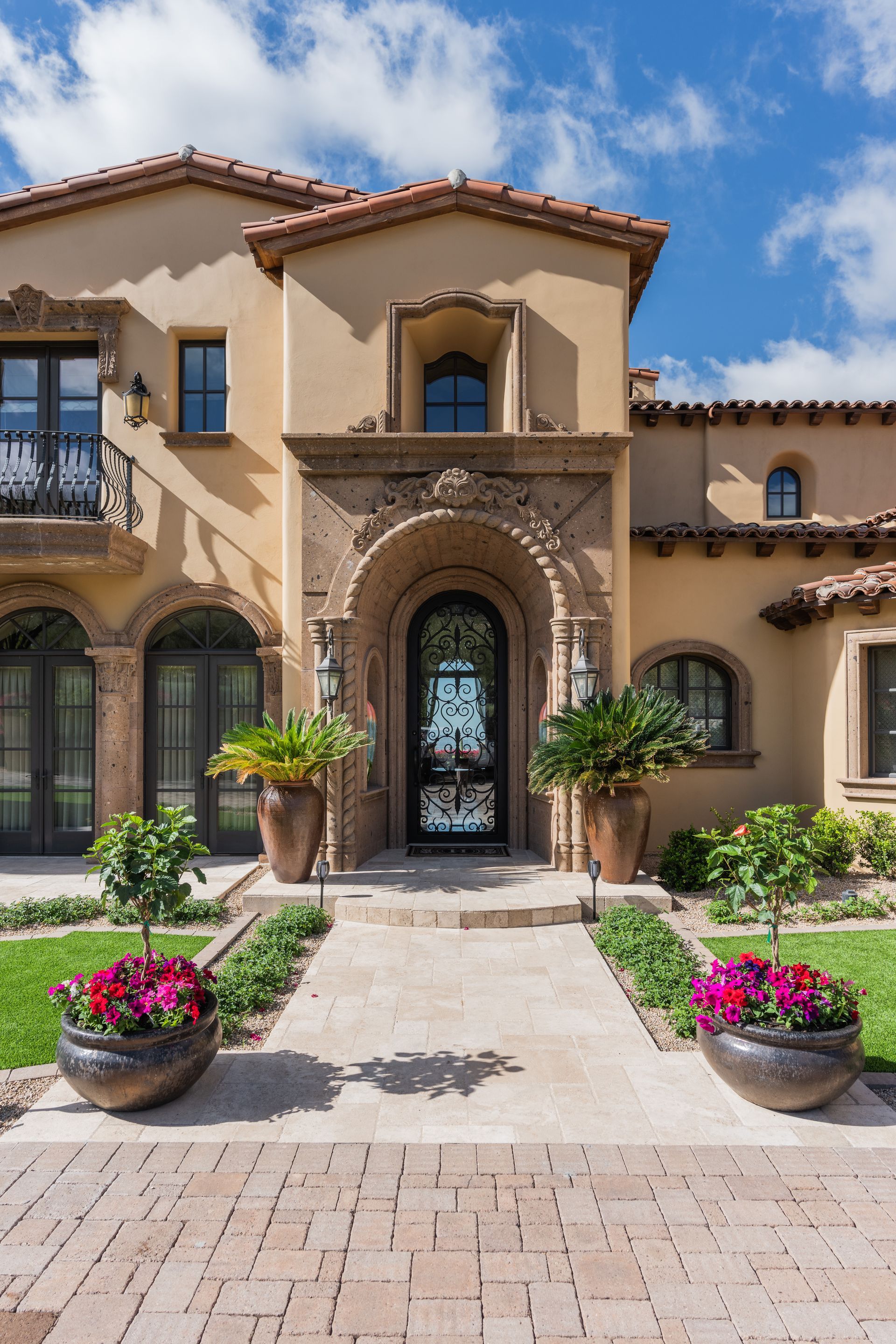 Mediterranean-style house with arched doorway, brick pathway, and potted plants.