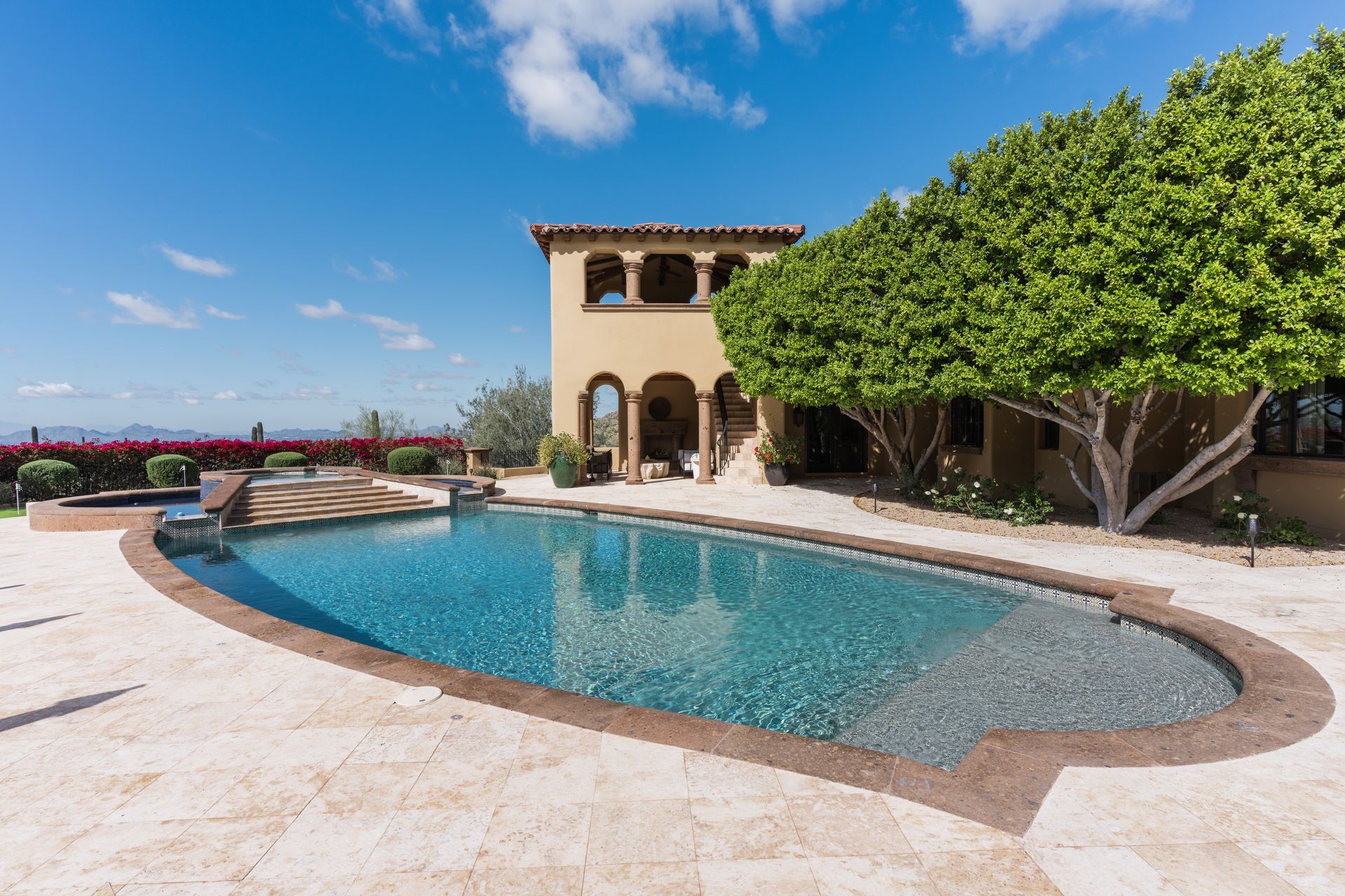 Poolside view of a multi-story home with a pool and lush landscaping under a blue sky.