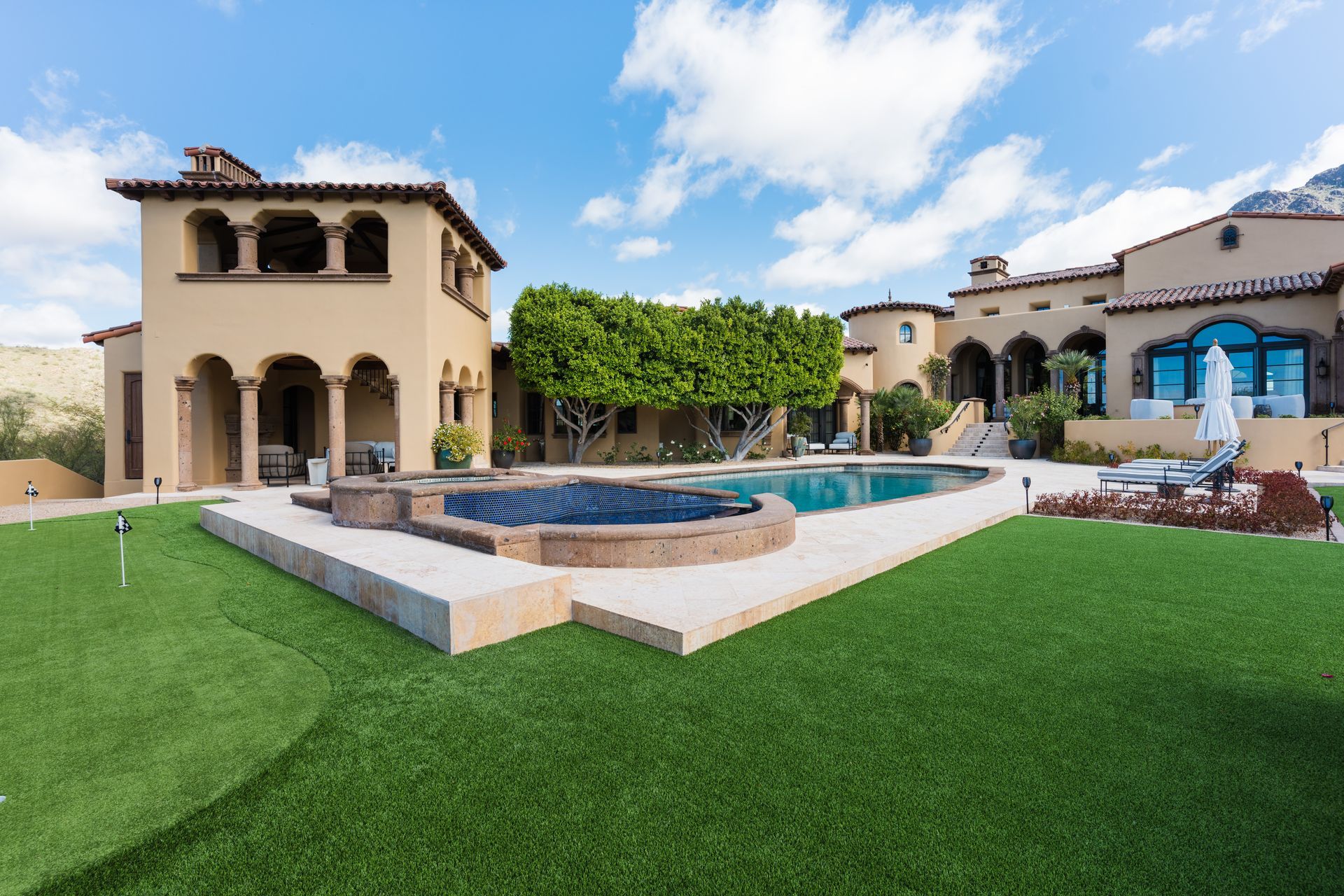 Mediterranean-style house with a pool, patio, and green lawn on a sunny day.