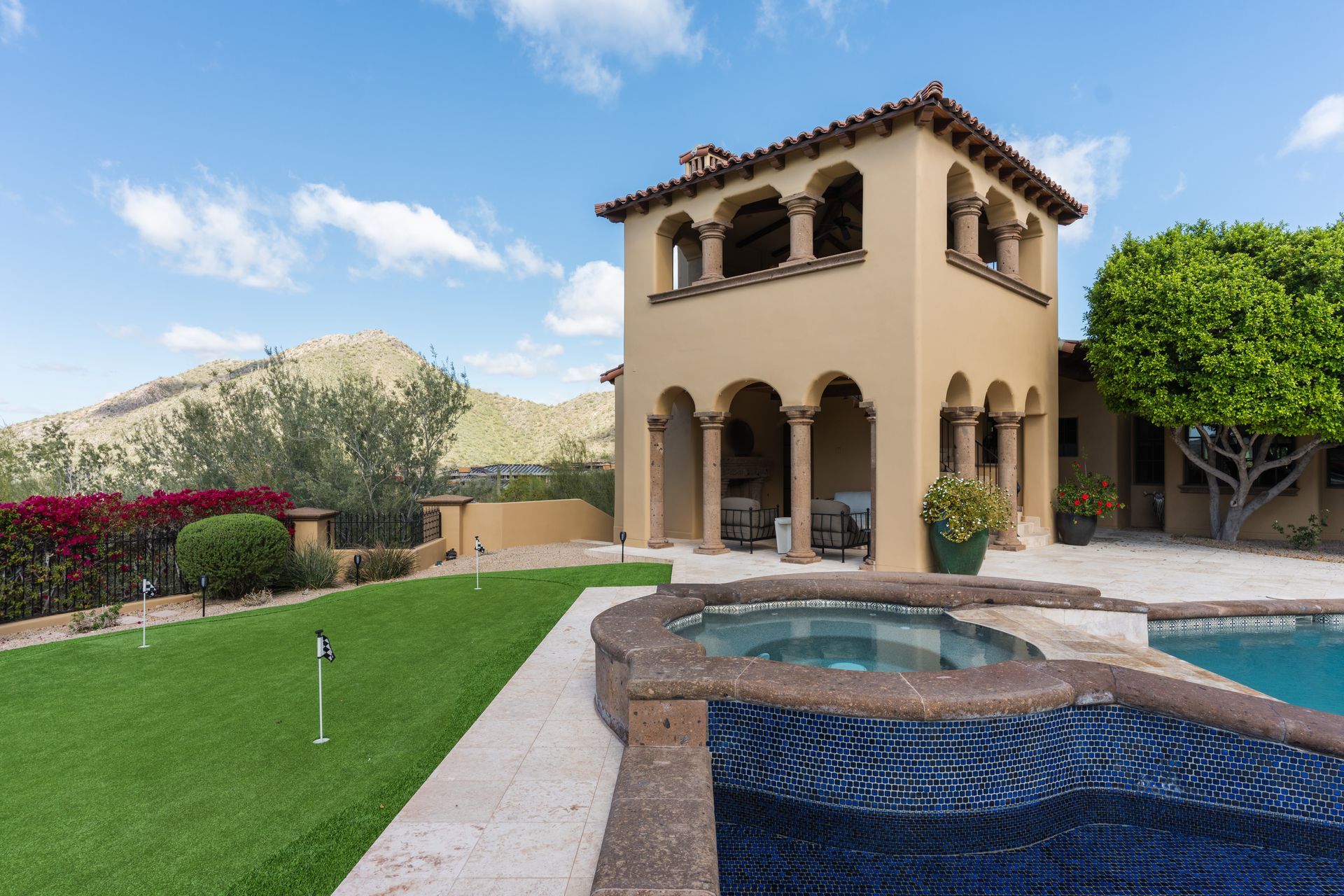 Luxury home exterior with a pool, spa, and tower overlooking a green lawn.