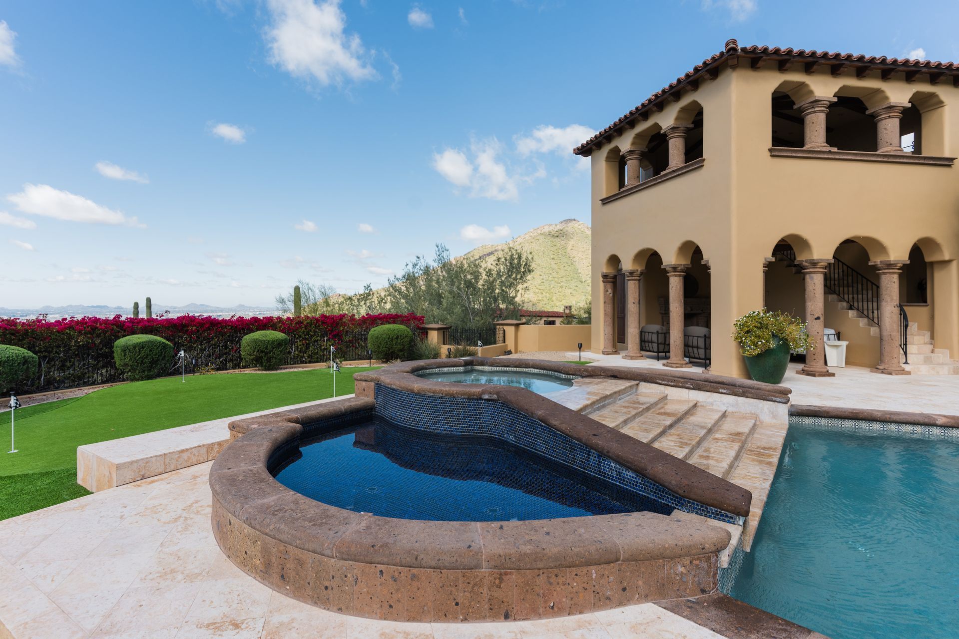 Luxury home exterior with pool, spa, and mountain view under blue sky.