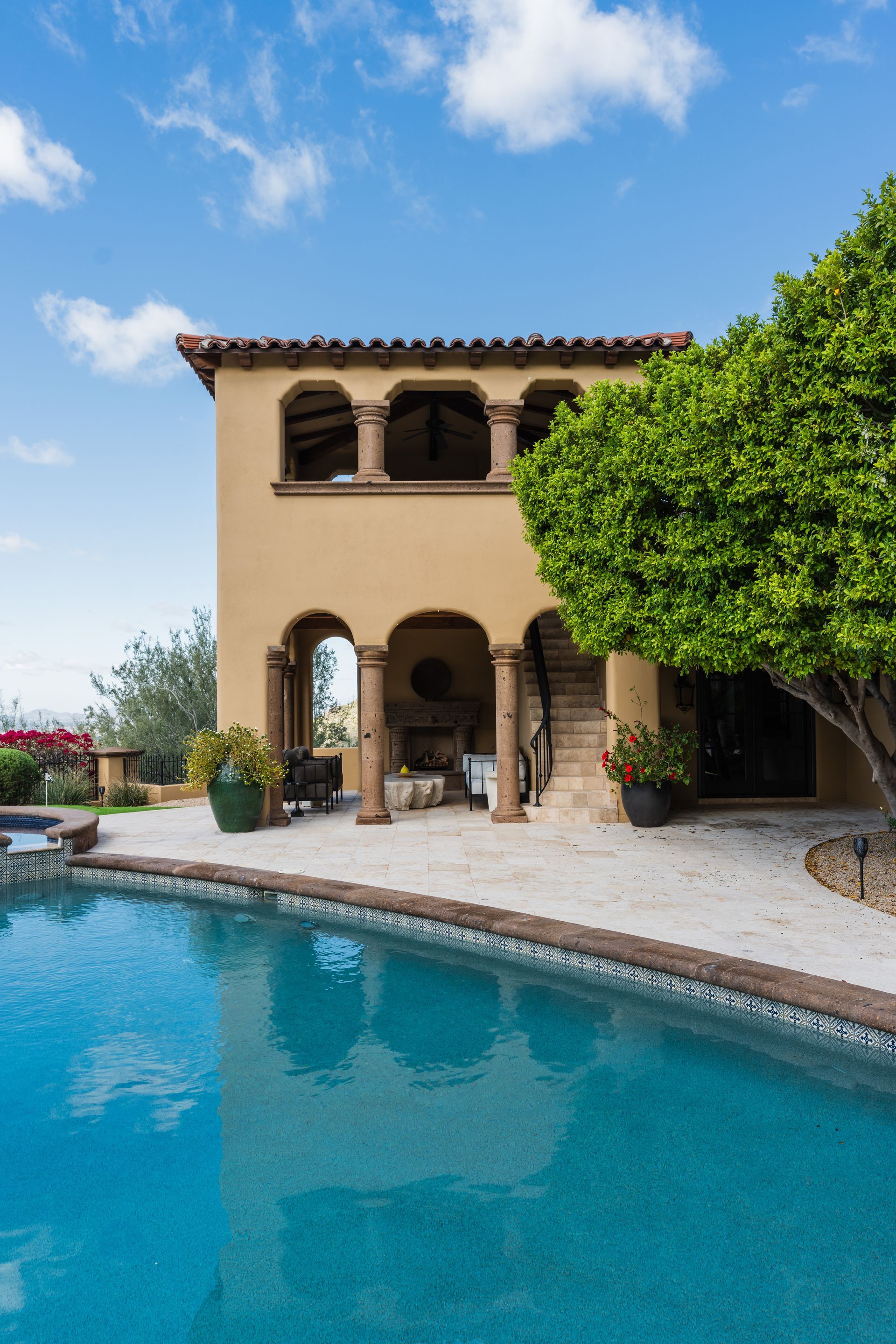Two-story building with arches and columns, overlooking a blue pool under a cloudy sky.