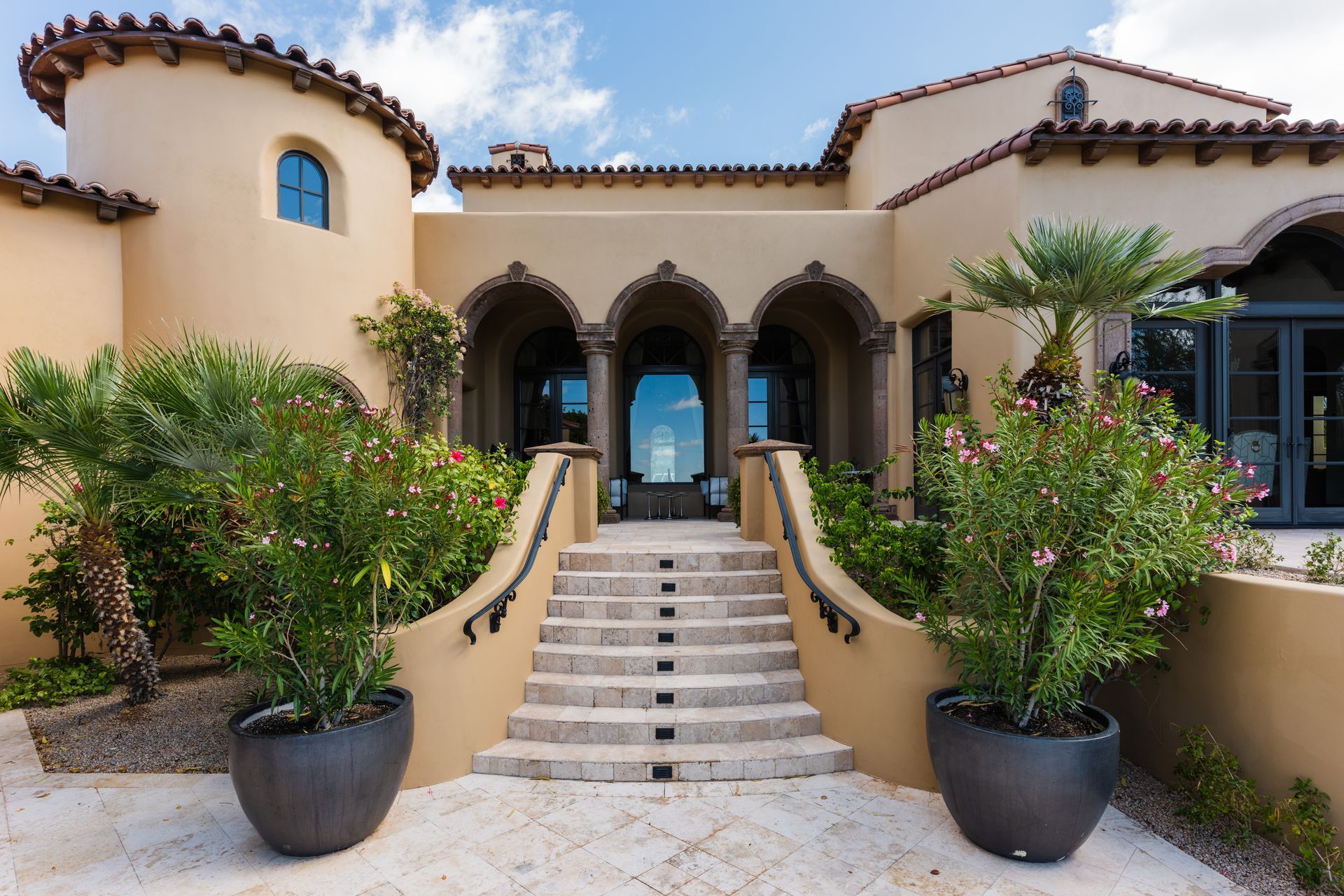 Beige stucco home with arched entryway, steps, and potted plants.