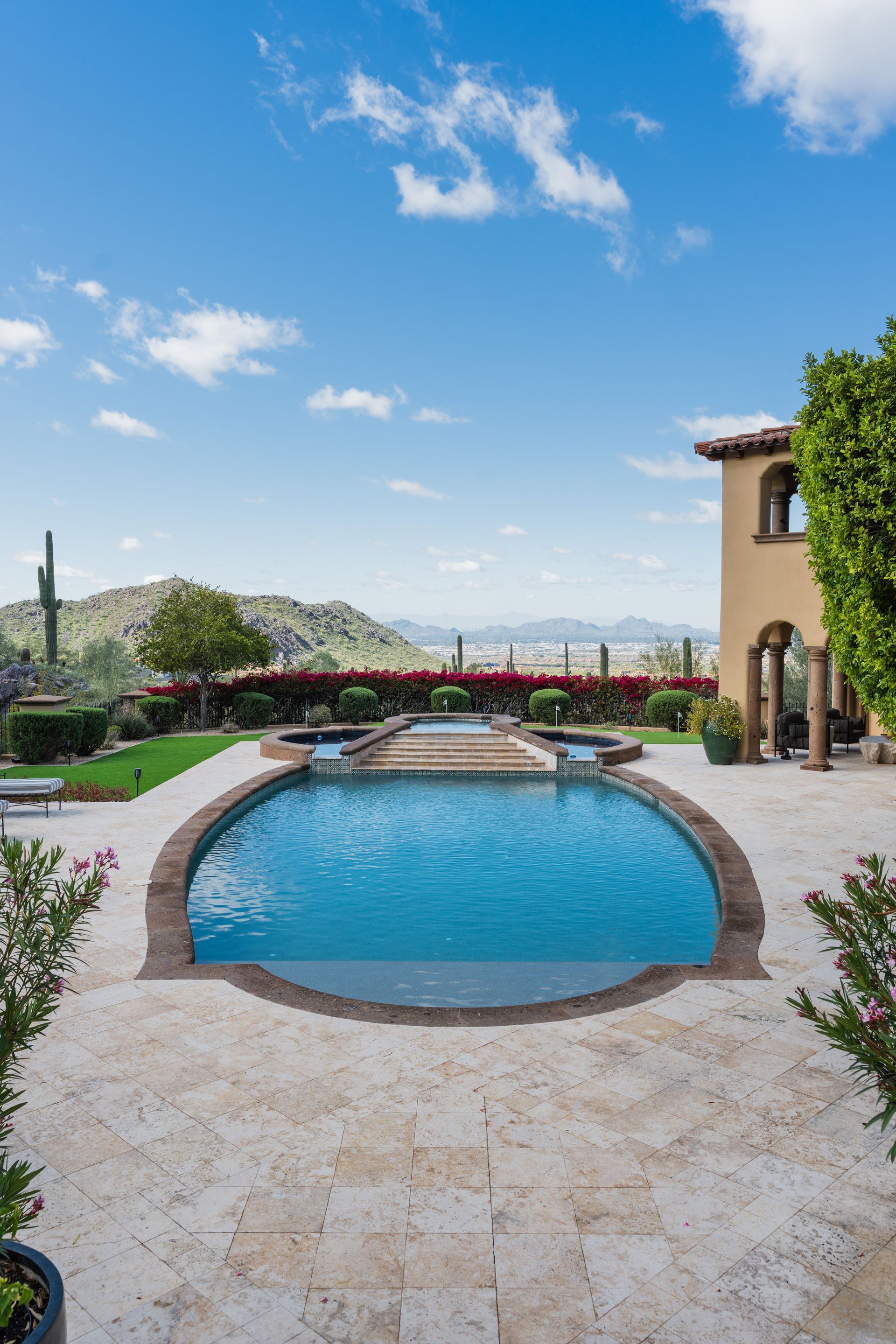 Pool in a luxurious backyard with a mountain view, under a partly cloudy blue sky.