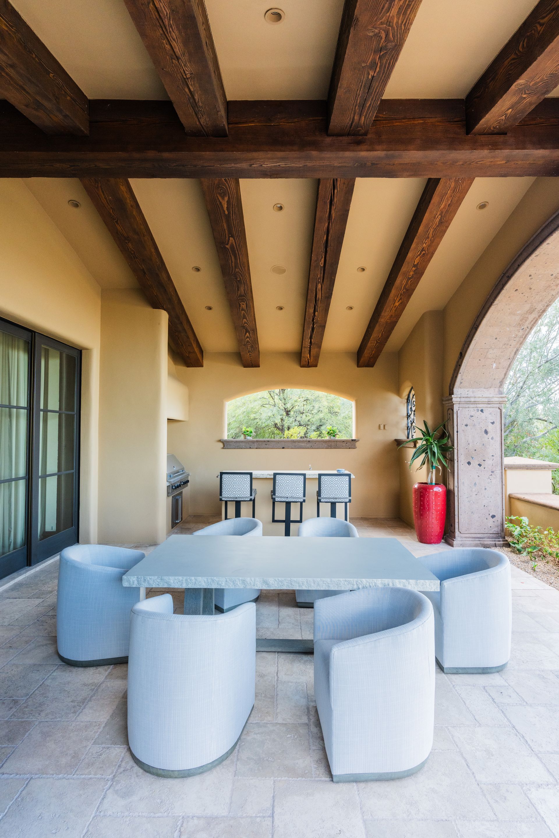 Patio with table and chairs under a wood-beamed ceiling, with an outdoor bar in the background.