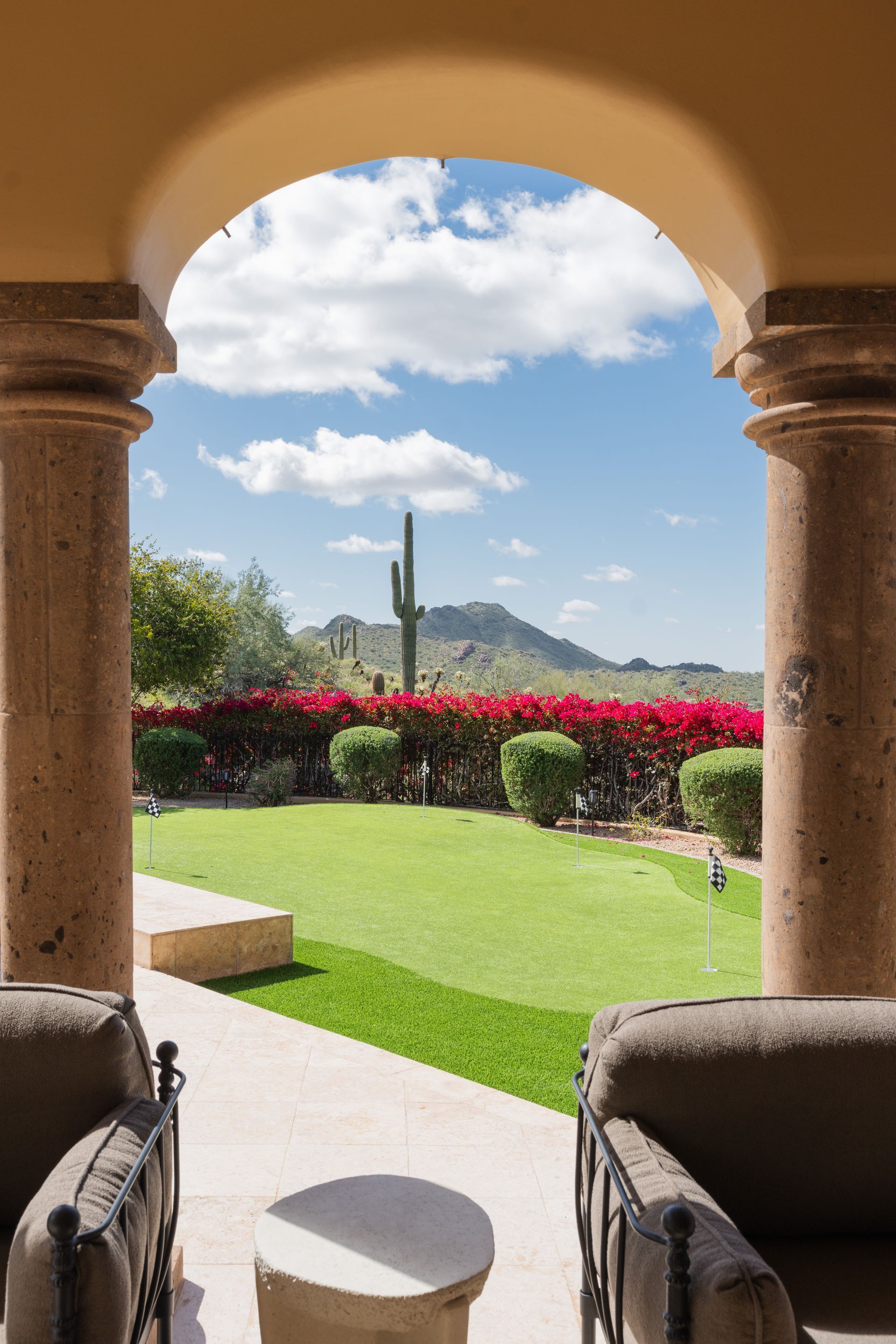 View through an archway of a manicured lawn, red flowers, and a mountain under a blue sky.