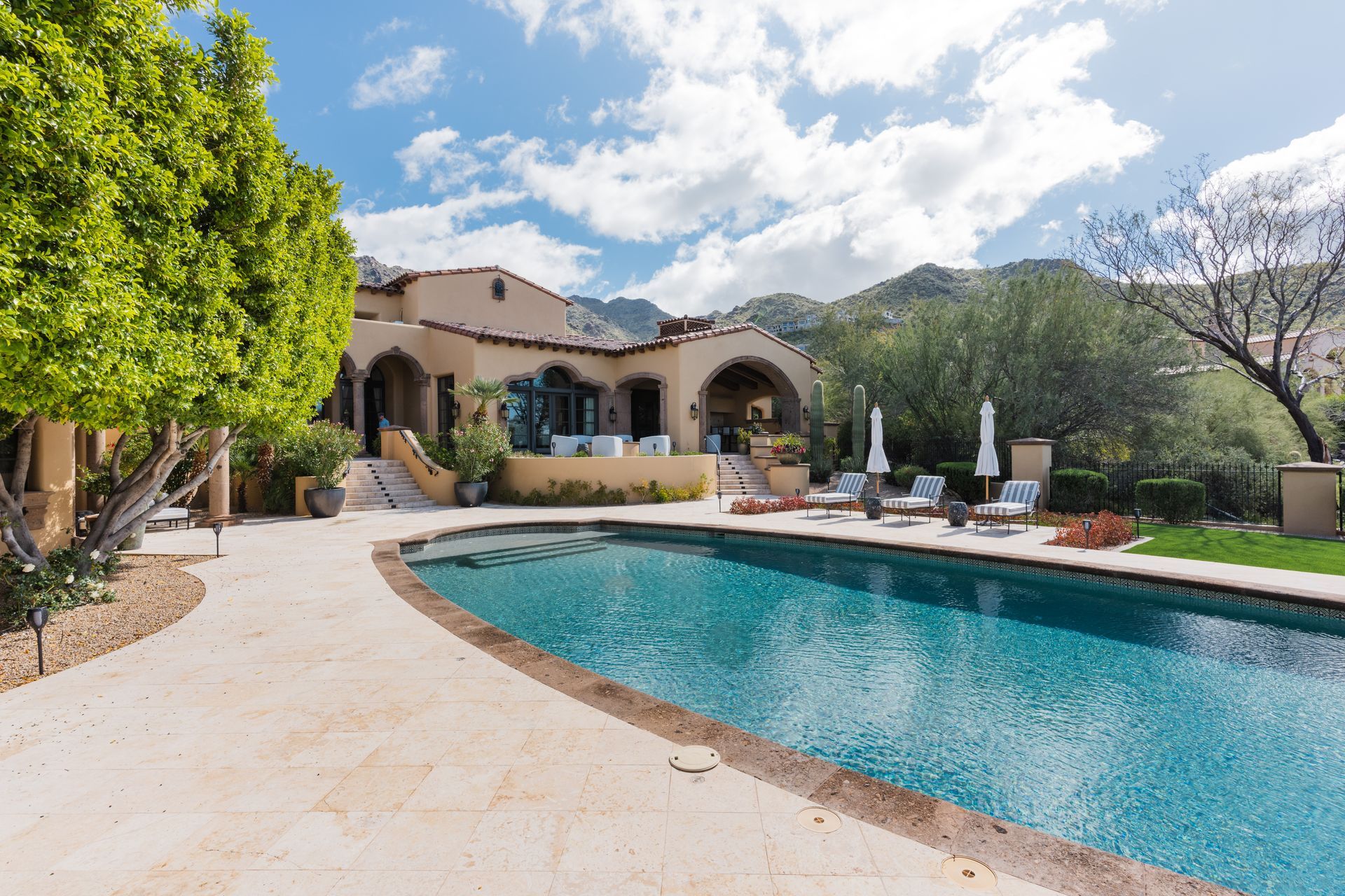 A luxurious home with a pool, lounge chairs, and mountain views.