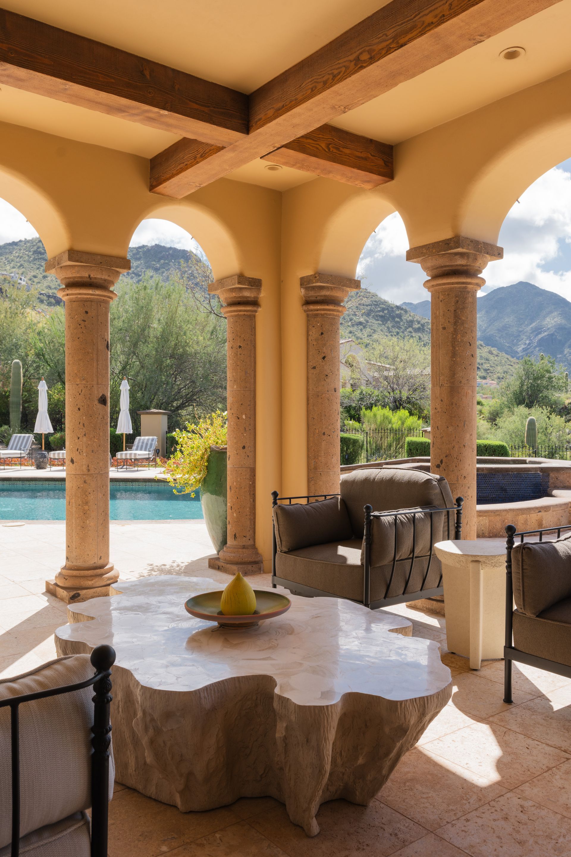 Covered patio with stone pillars, a unique stone table, and mountain view overlooking a pool.