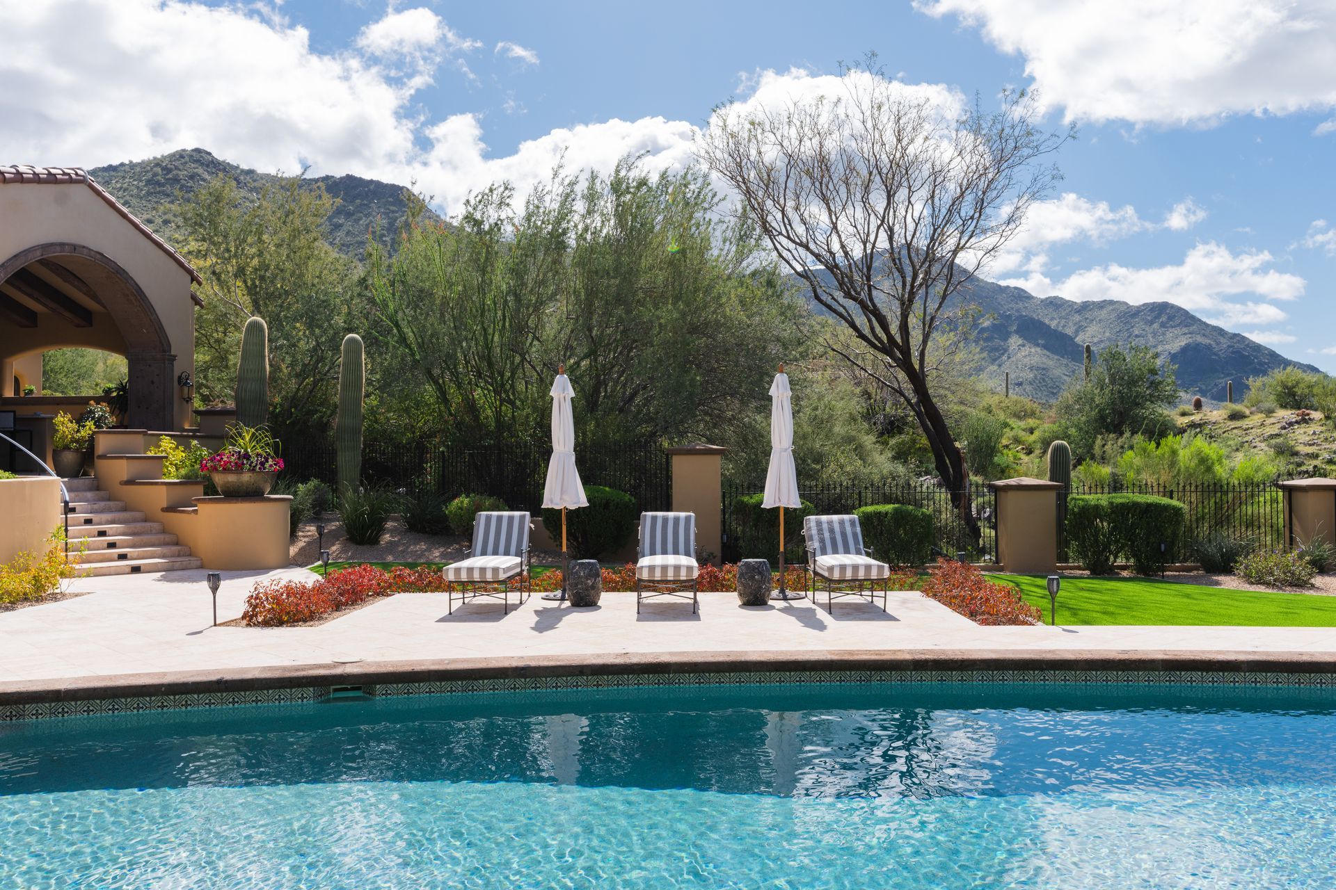Poolside scene with striped chairs, umbrellas, and mountain backdrop.