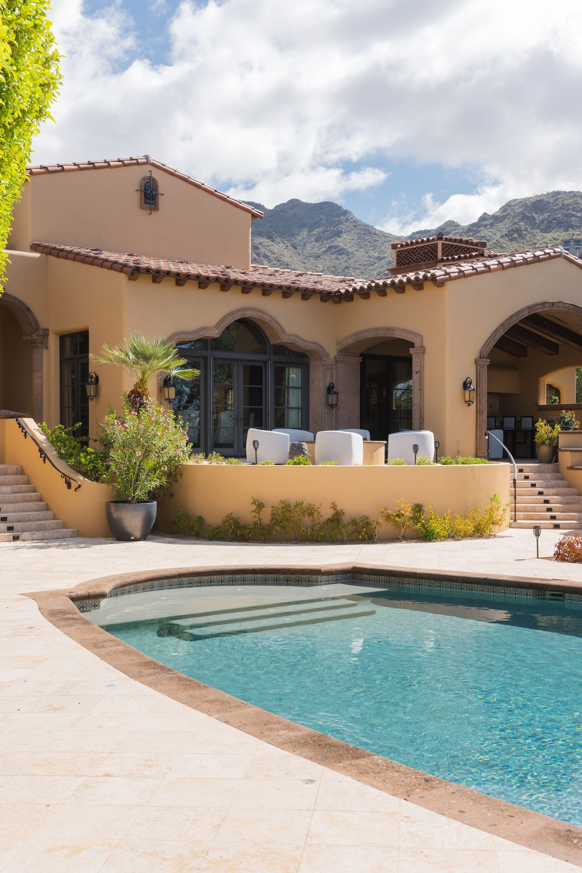 Spanish-style home with a turquoise pool, patio, and mountain backdrop.
