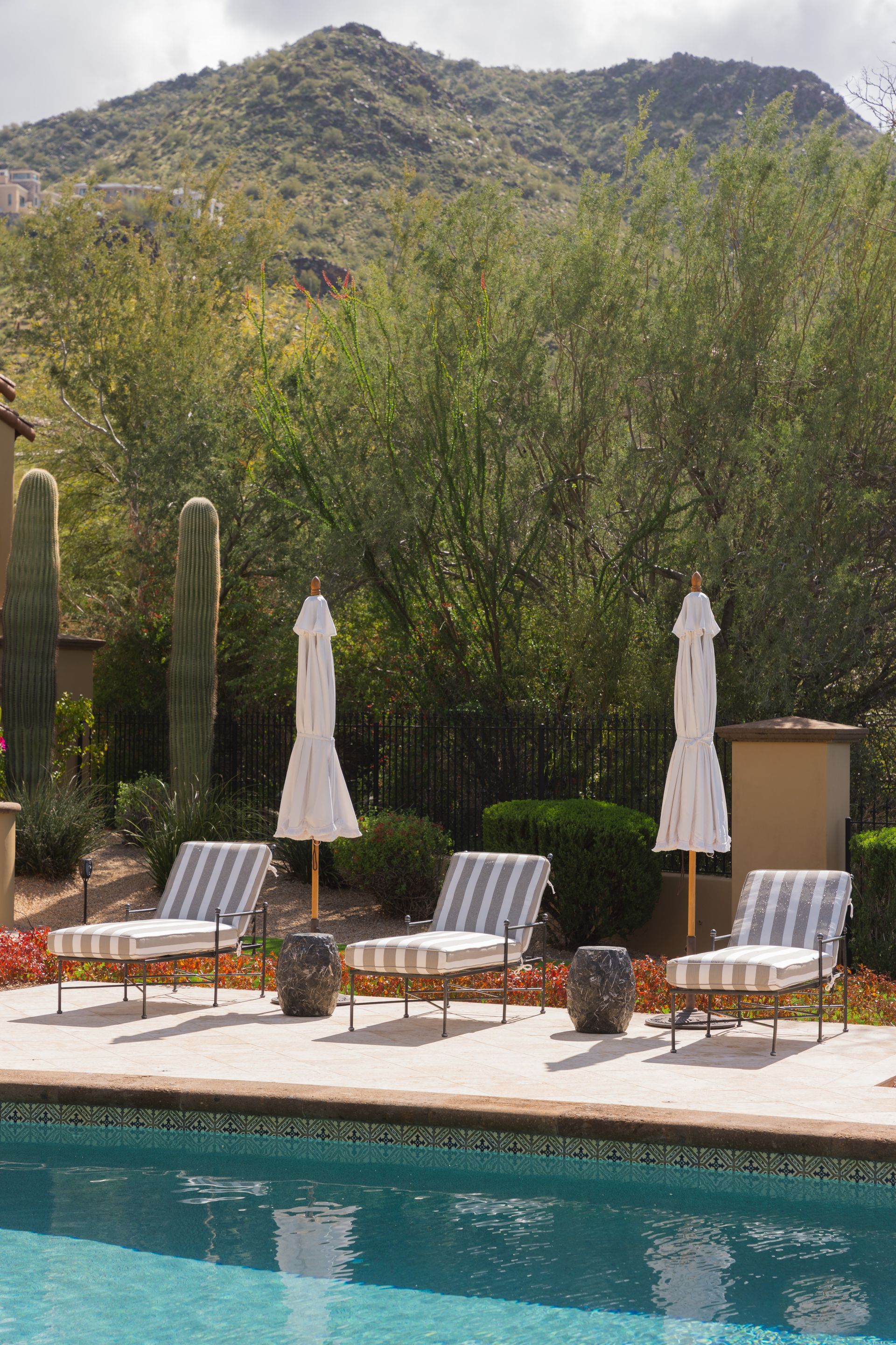 Poolside scene with striped lounge chairs, umbrellas, and mountain backdrop.