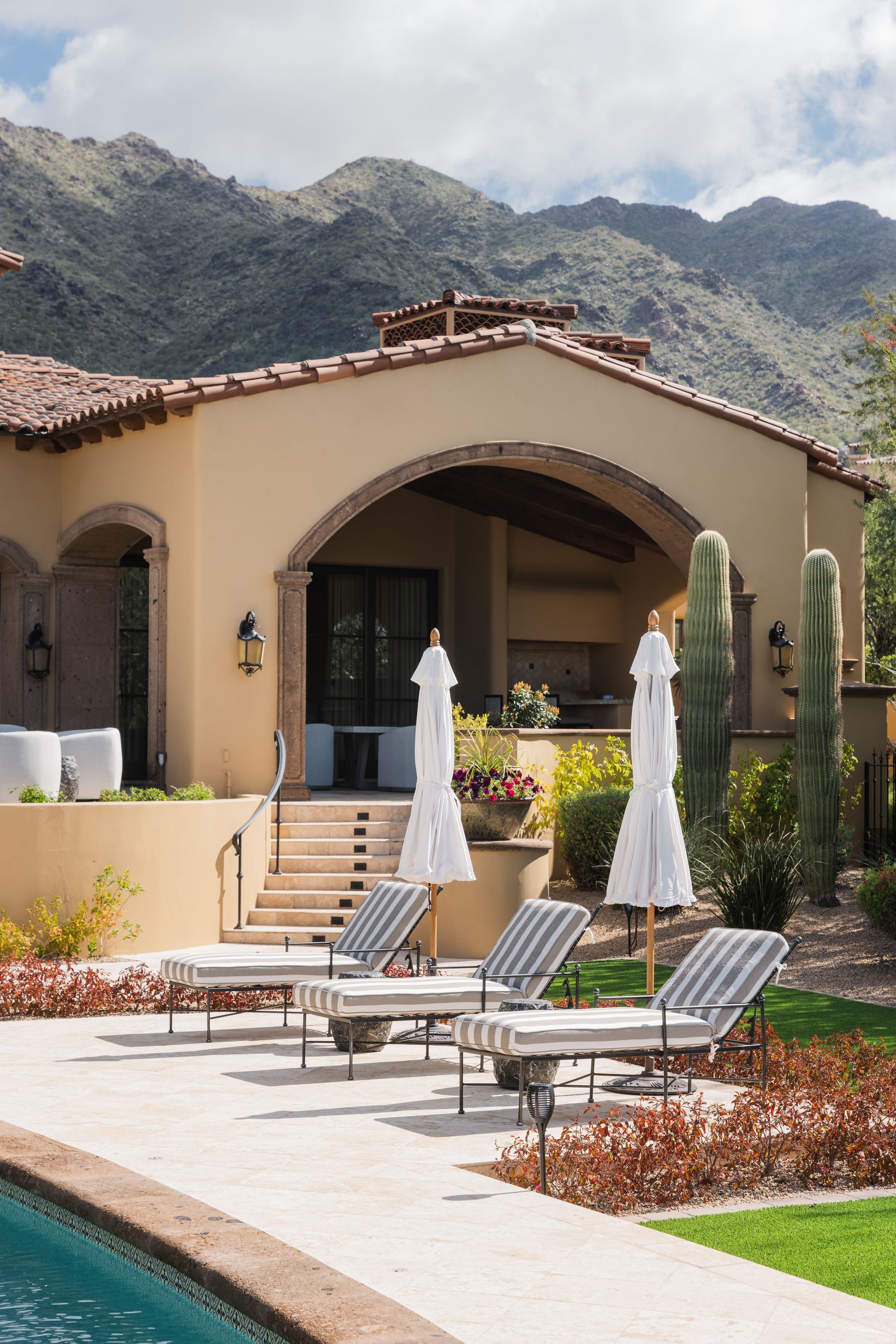 Poolside patio with chaise lounges, umbrellas, and mountain backdrop.