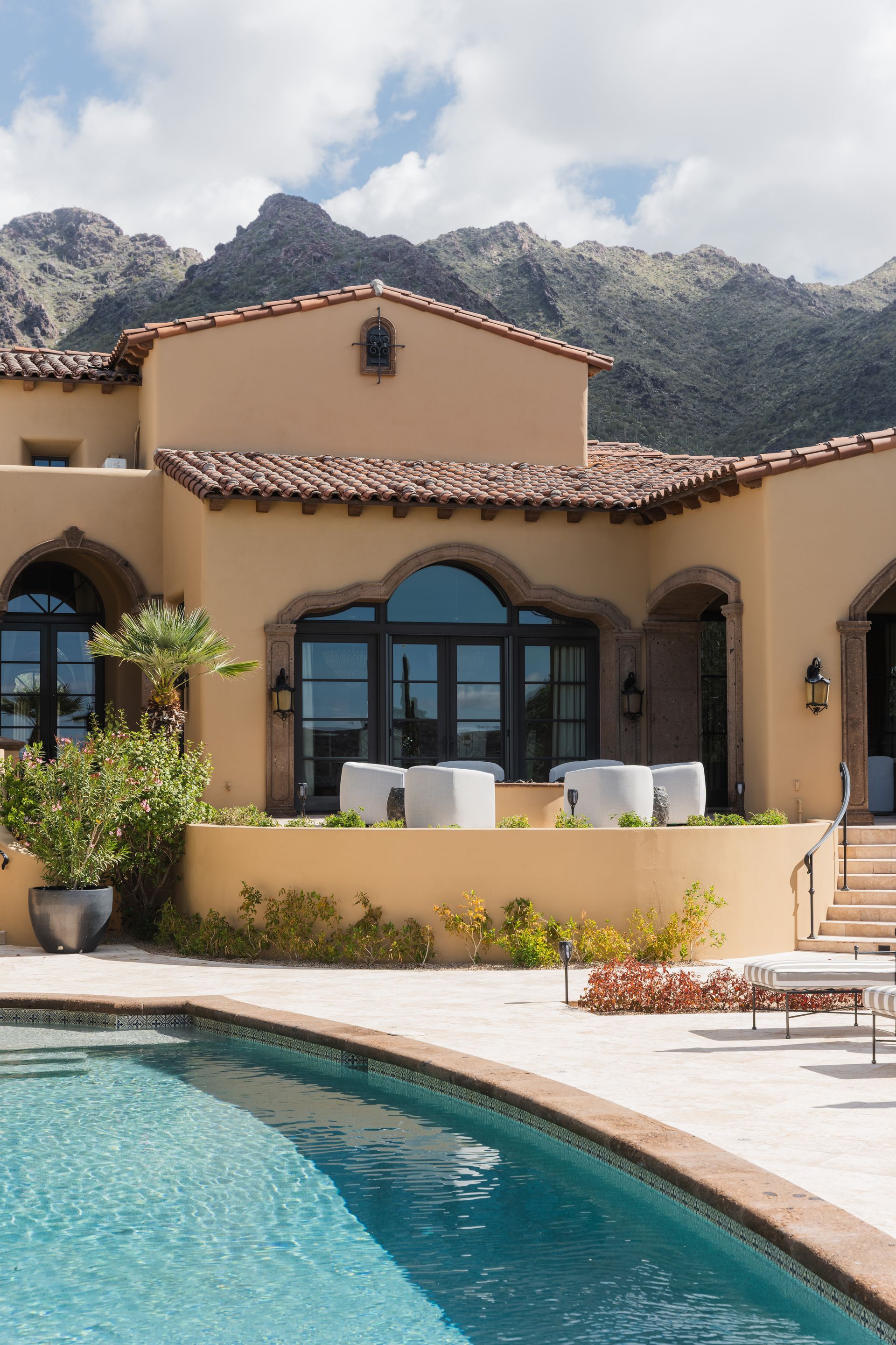 Beige stucco house with terracotta roof, pool, and mountain backdrop.