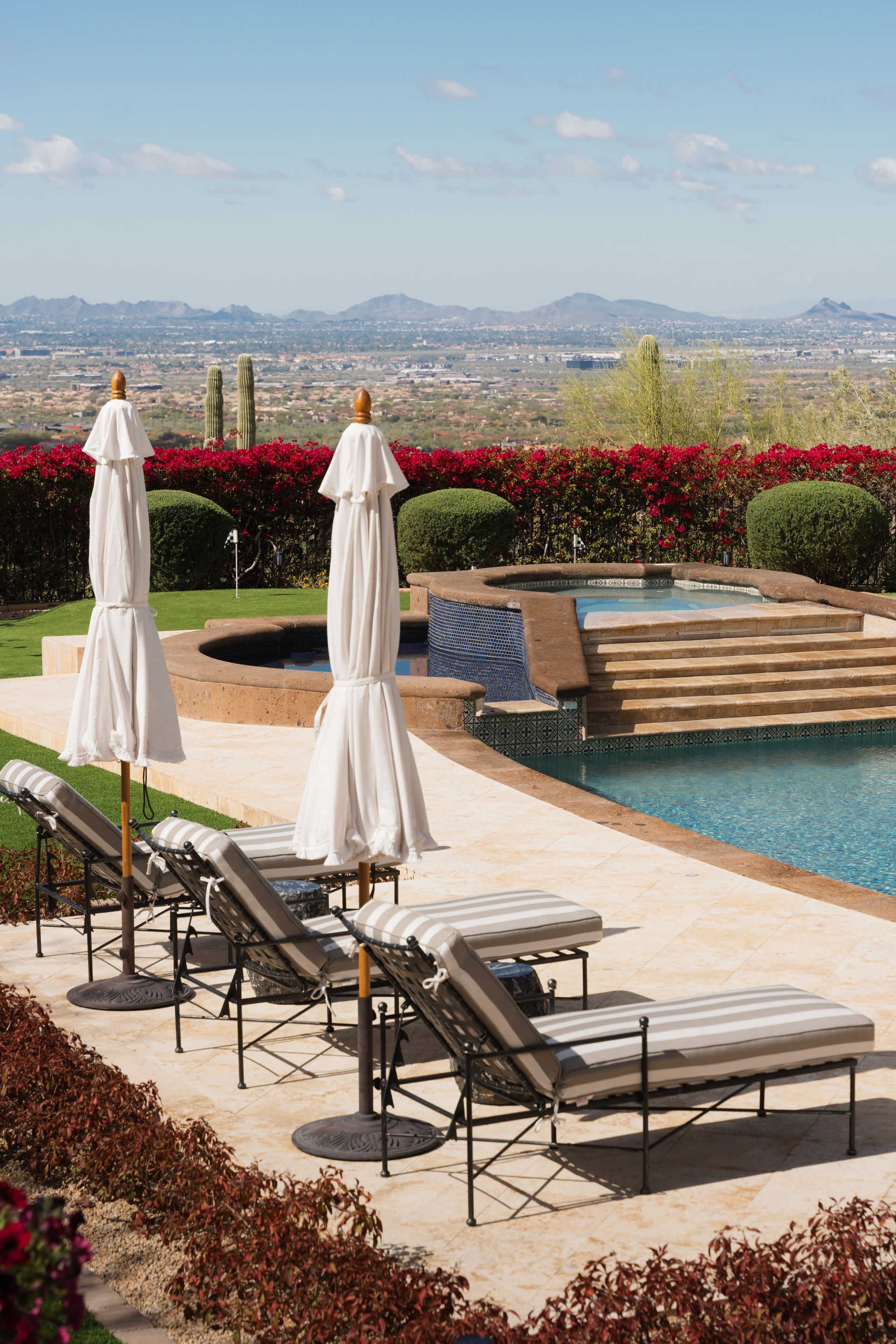 Poolside scene: lounge chairs under umbrellas, overlooking a pool and cityscape with a mountain backdrop.