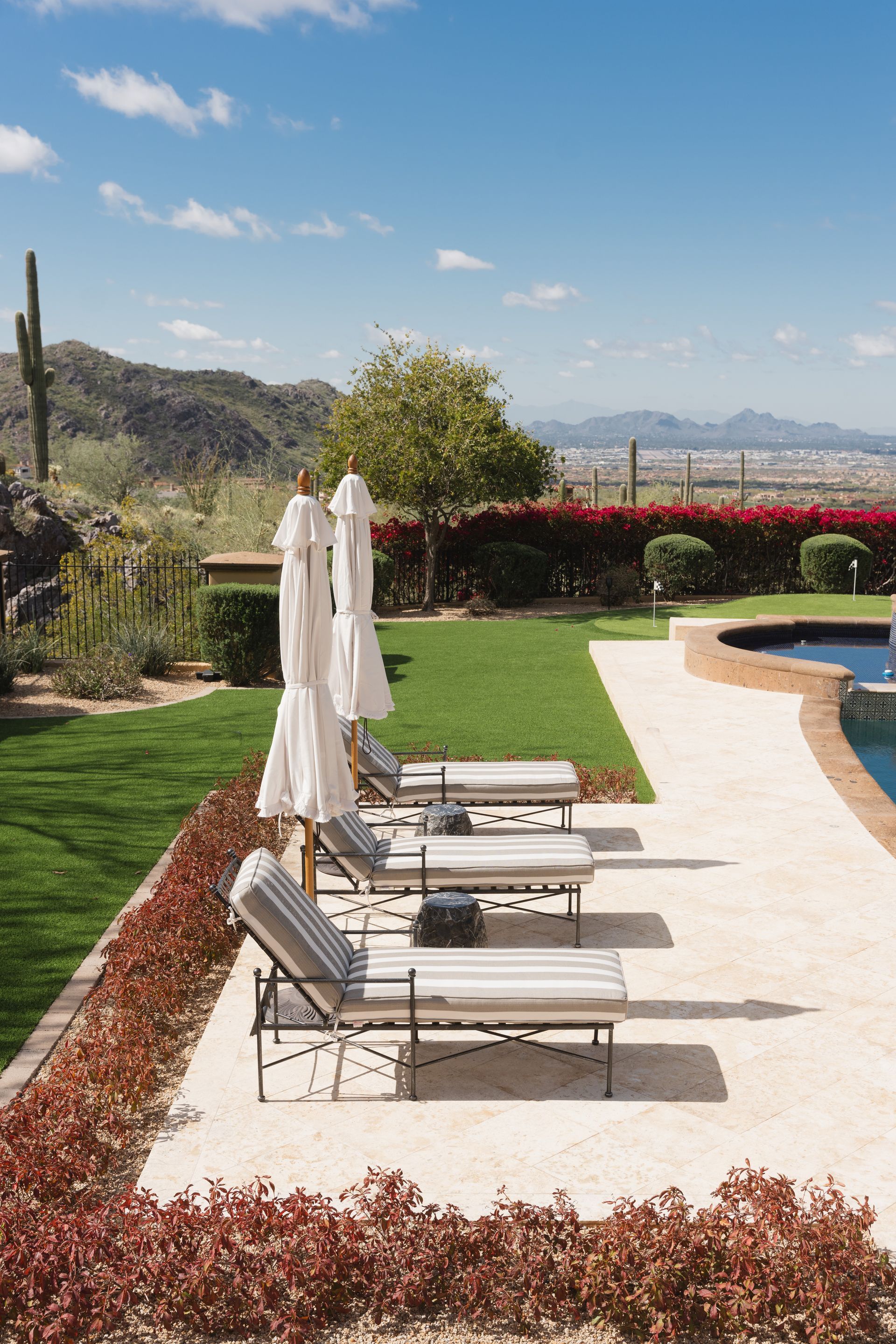 Lounge chairs with umbrellas by a pool overlook a desert landscape on a sunny day.