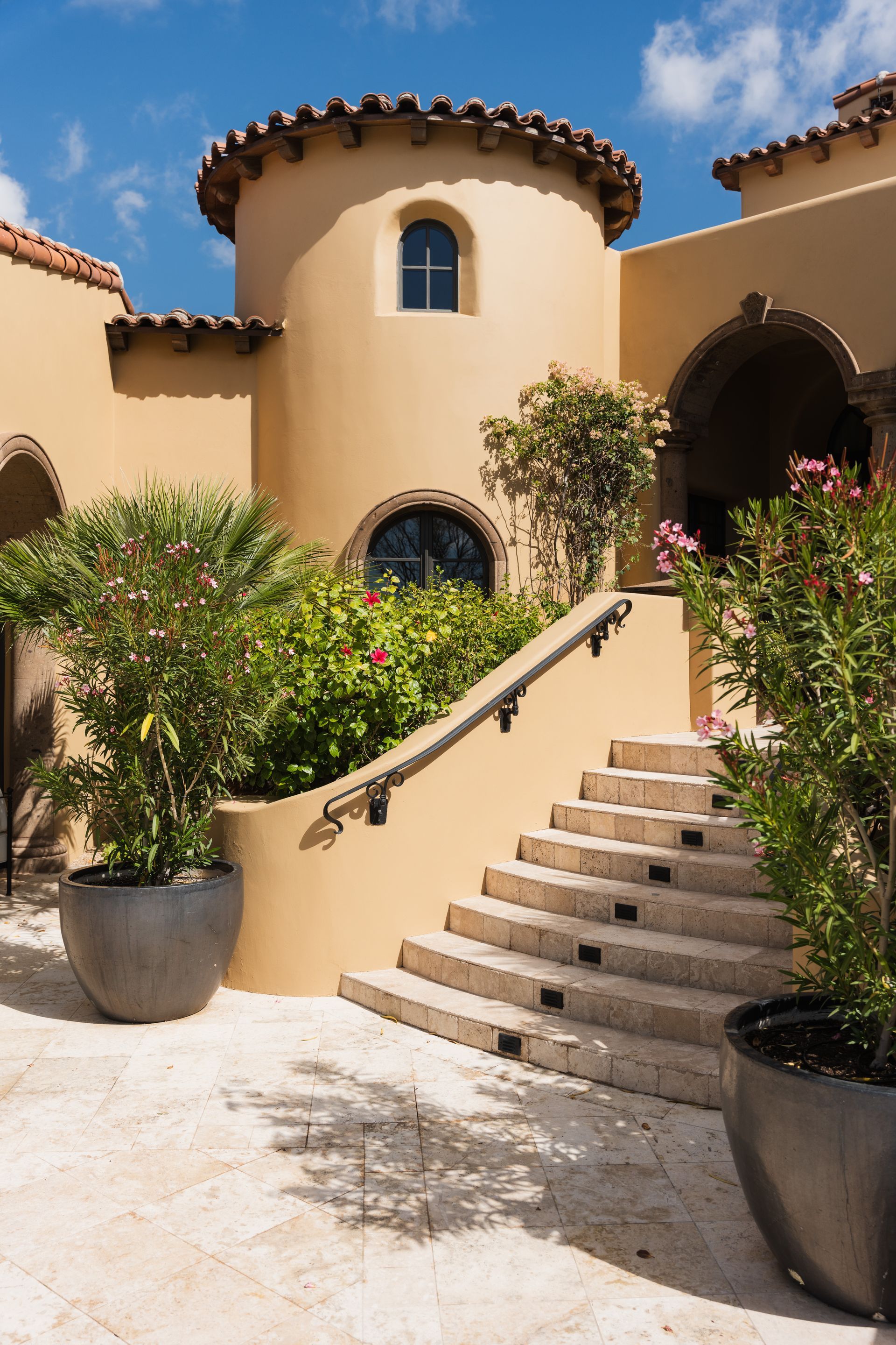 Stone steps lead to a tan building with a turret and potted plants.