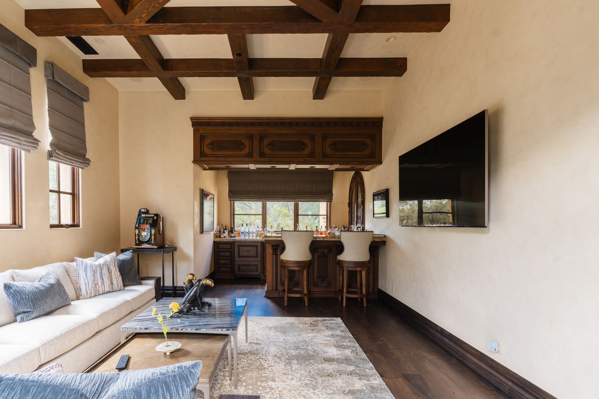 Living room with a bar, cream walls, wood beams, a white sofa, and a television.