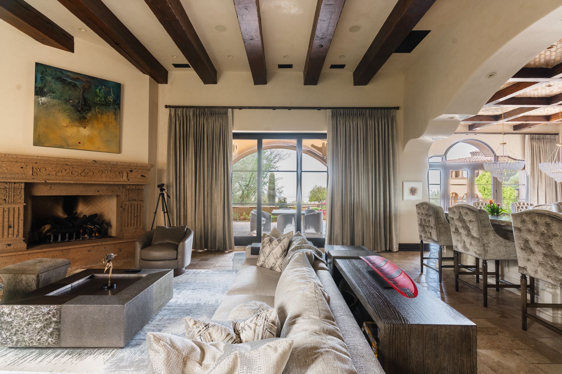 Living room with fireplace, arched doorway, and dark wood beams. Furnished with a sofa, chairs, and dining table.