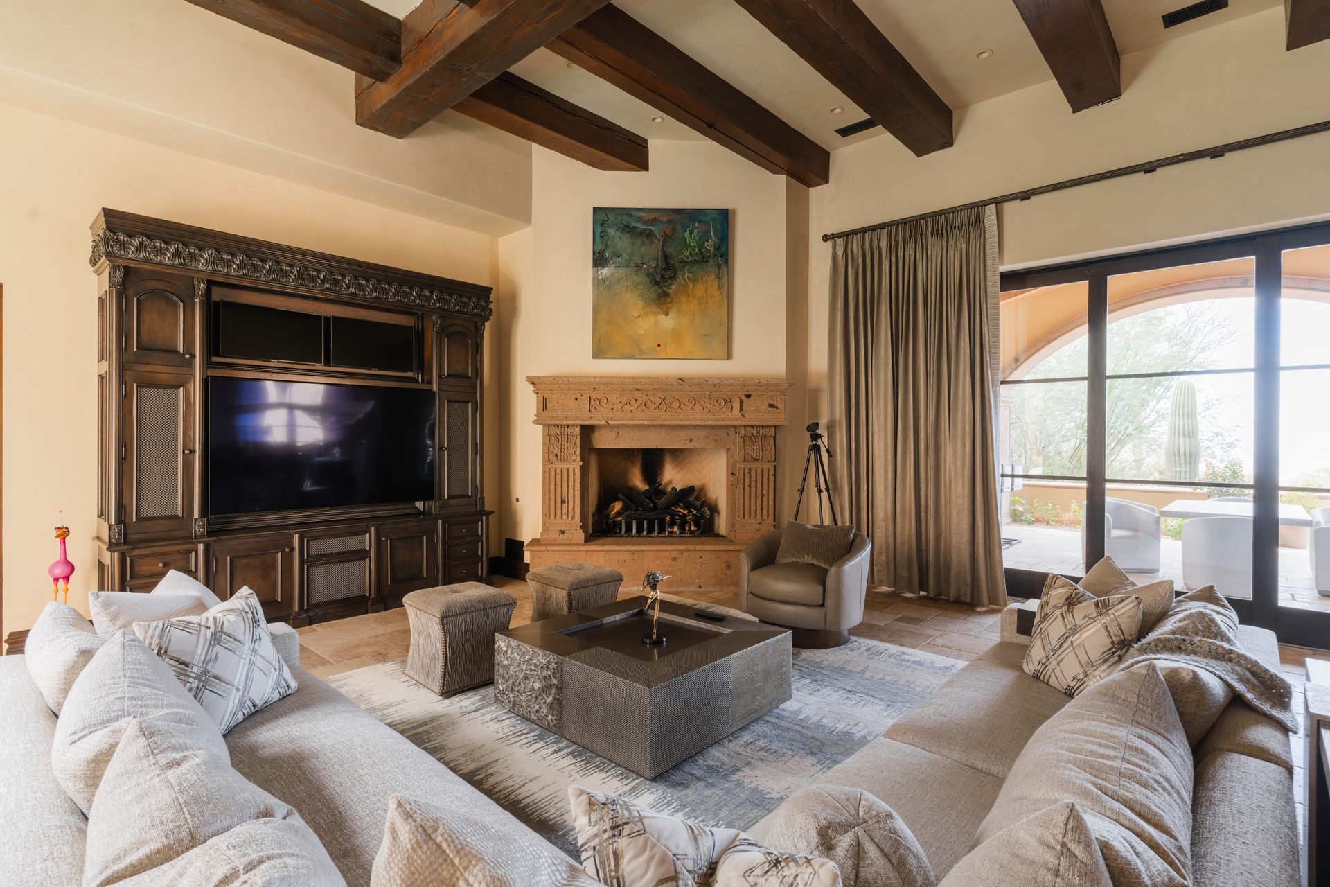 Spacious living room with a stone fireplace, large TV cabinet, sectional sofa, and exposed wooden beams.
