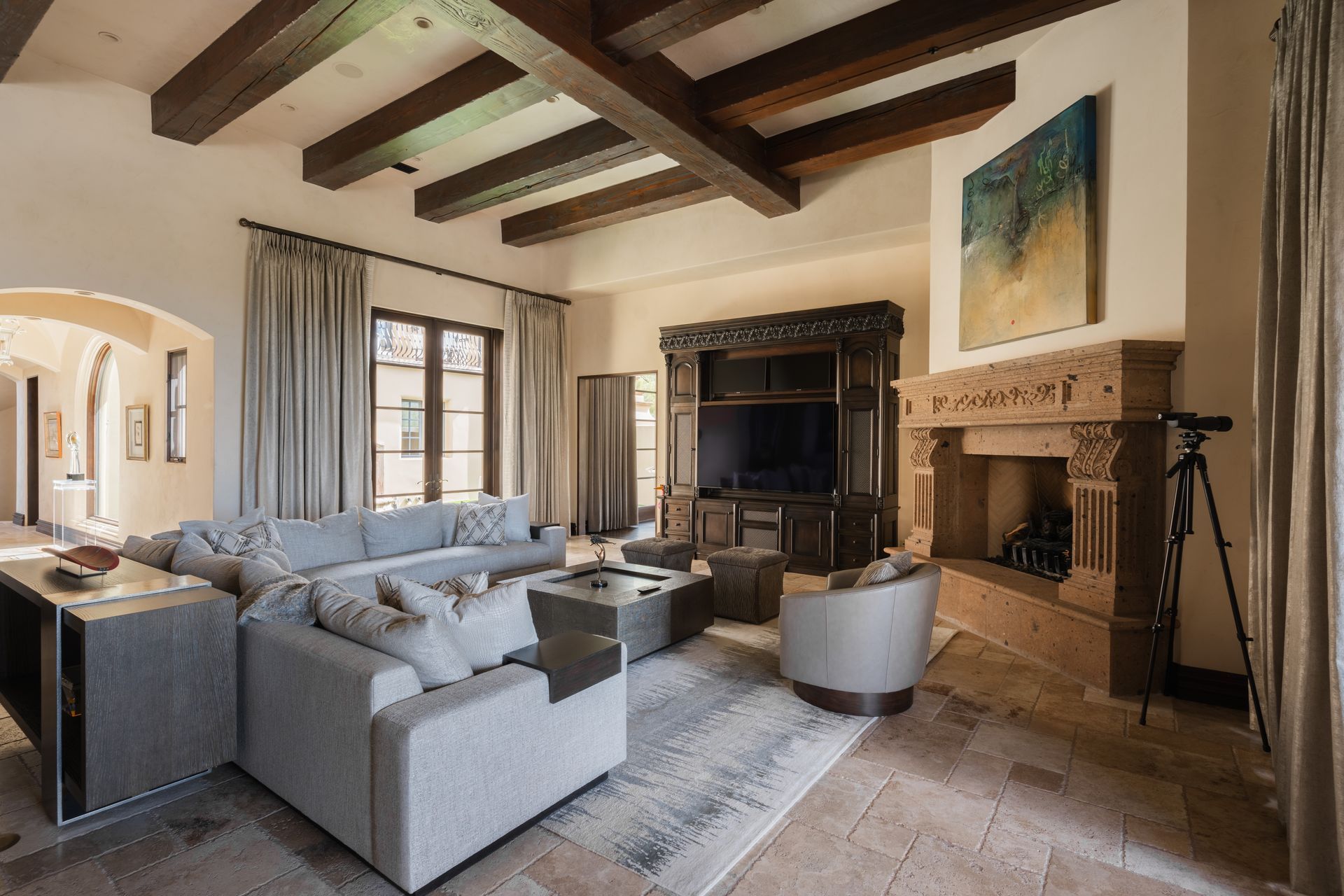 Spacious living room with stone fireplace, wooden beams, sectional sofa, and a large TV cabinet.