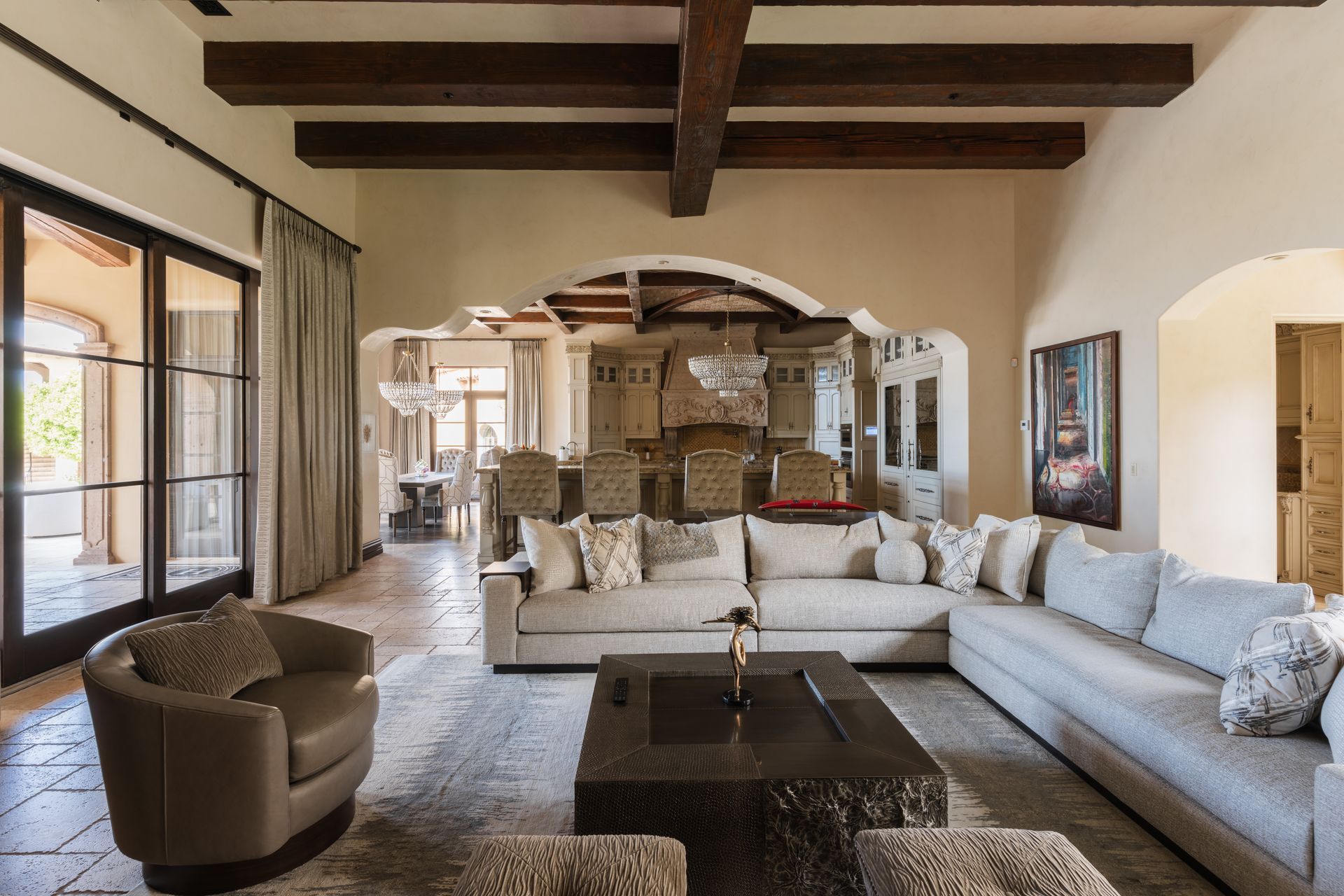Living room with beige sectional sofa, dark wood beams, and open doorway to dining area.