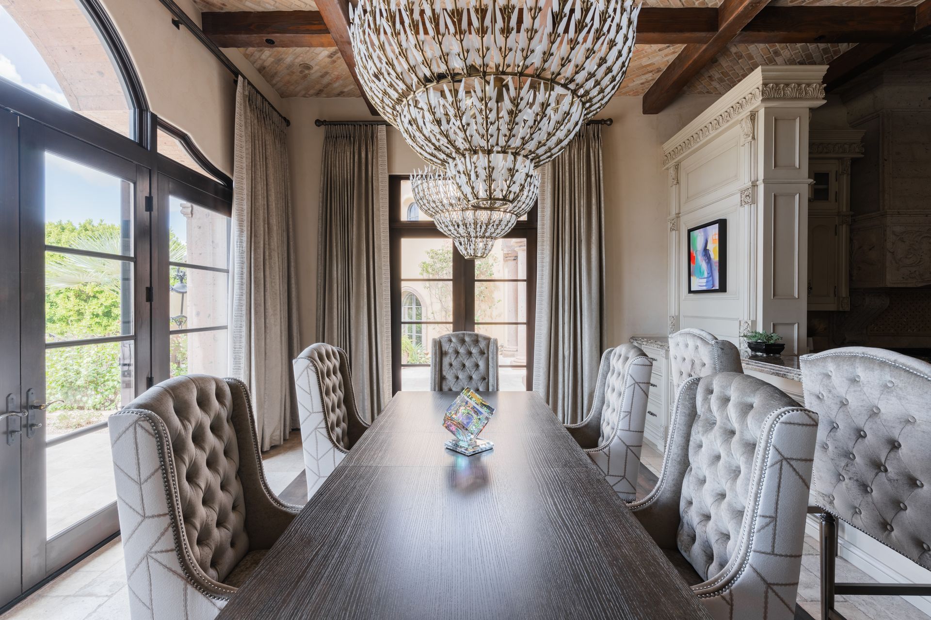Dining room with a long table, tufted chairs, and crystal chandeliers.