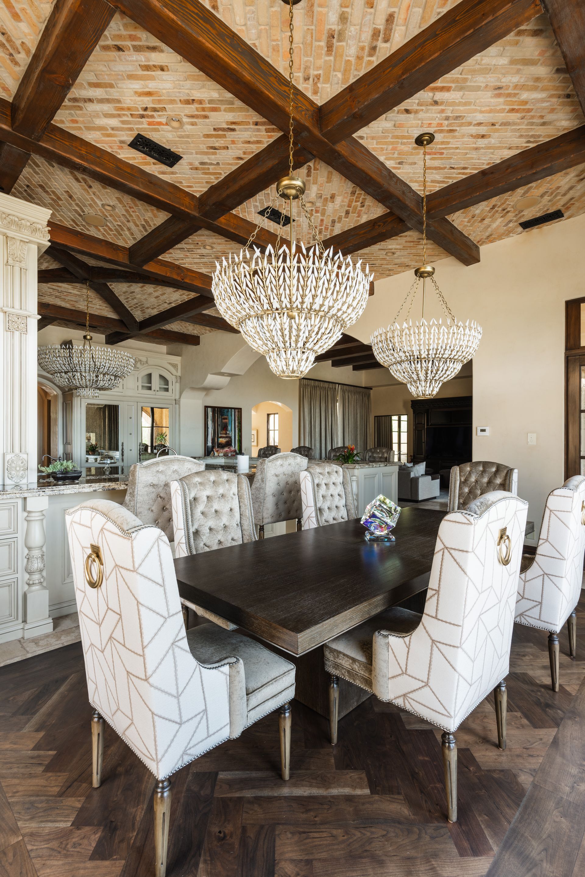 Elegant dining room with chandelier lighting, wood ceiling beams, and patterned chairs.