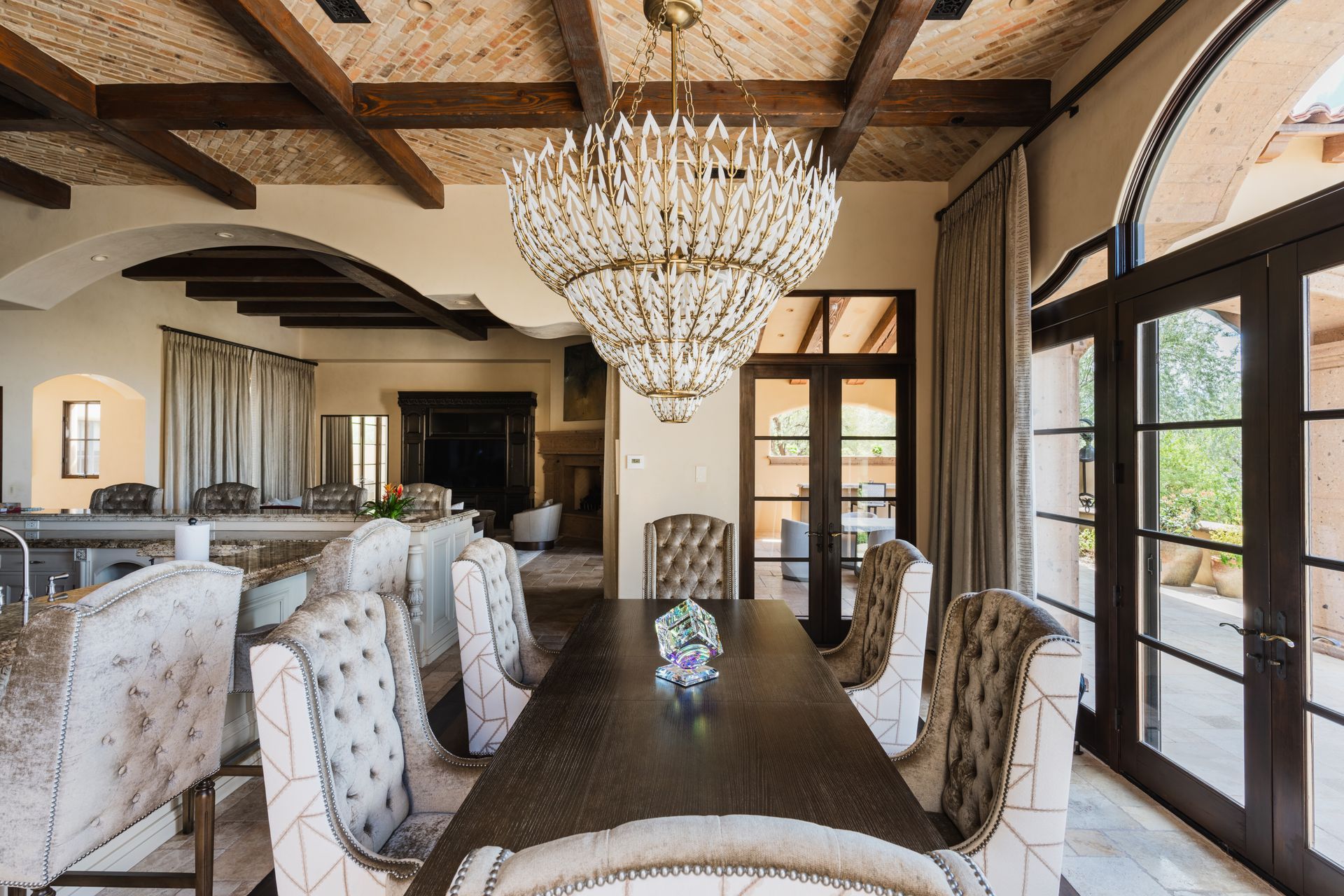 Dining room with large chandelier, dark wooden table, and tufted chairs.