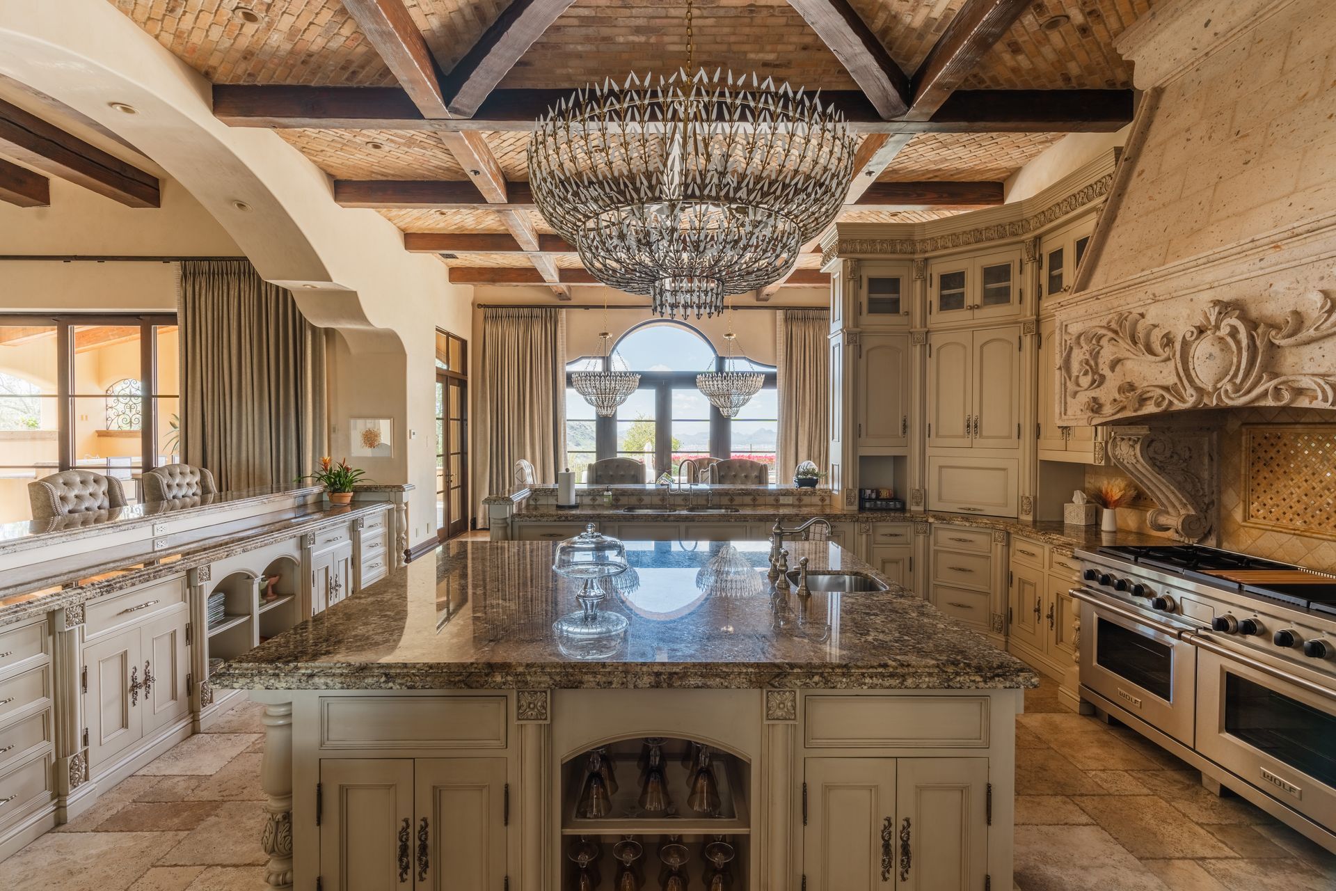 Elegant kitchen with a large island, chandelier, ornate cabinets, and a view to a dining area.