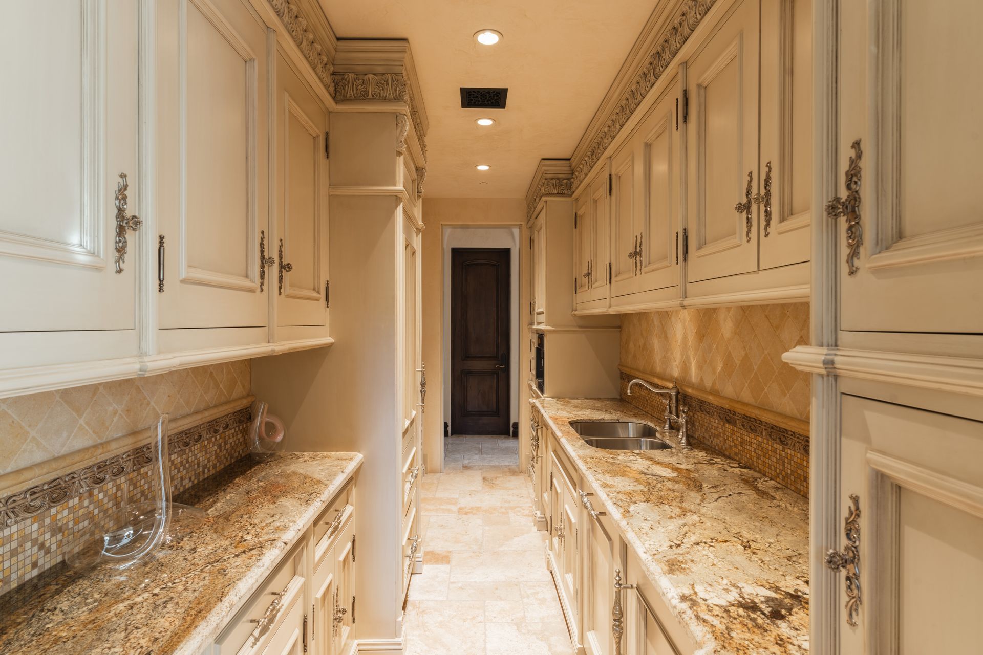 Narrow, well-lit kitchen with cream-colored cabinets, granite countertops, and a small sink.
