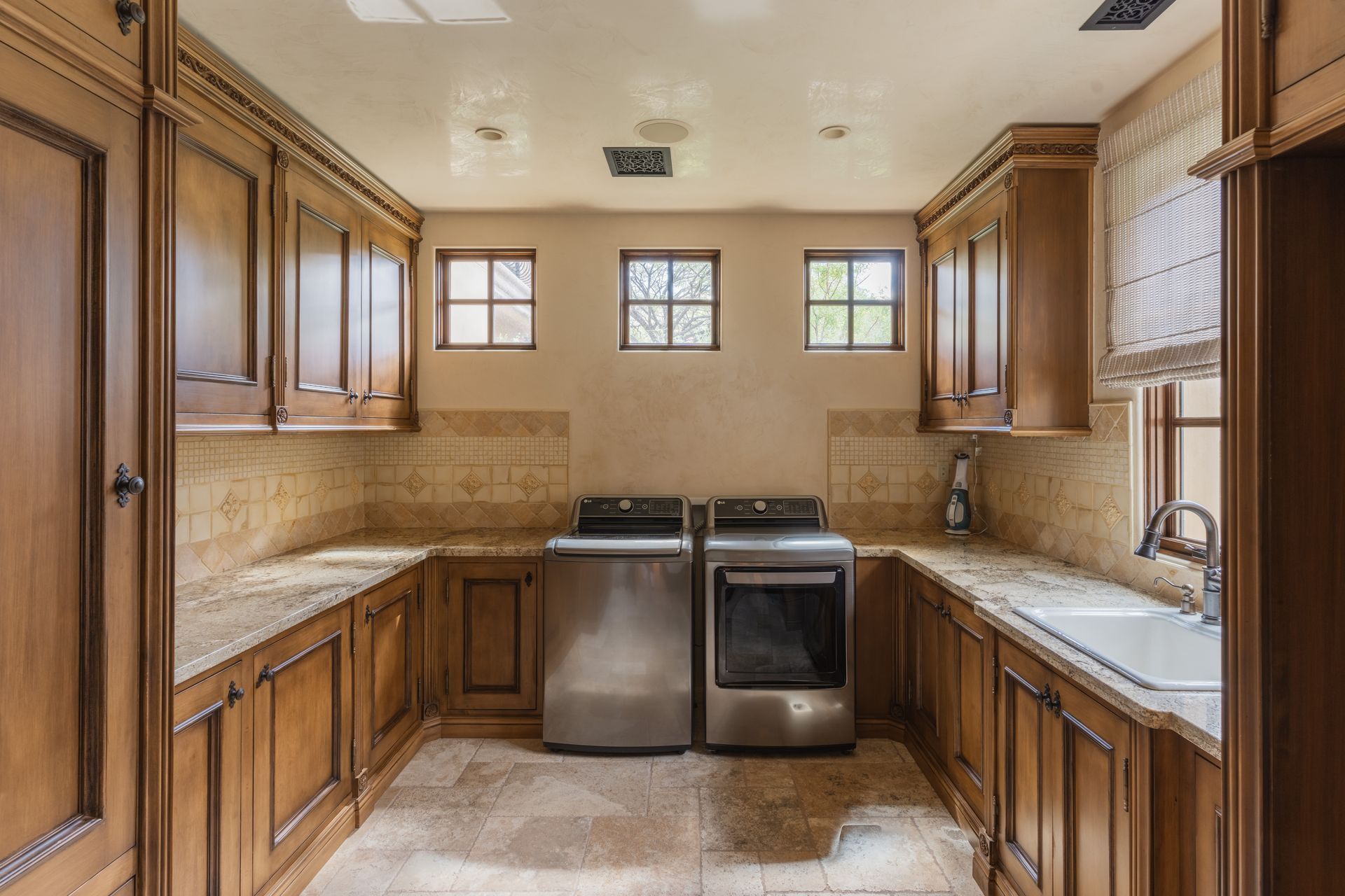 Laundry room with wood cabinets, stone countertops, stainless steel appliances, and small windows.