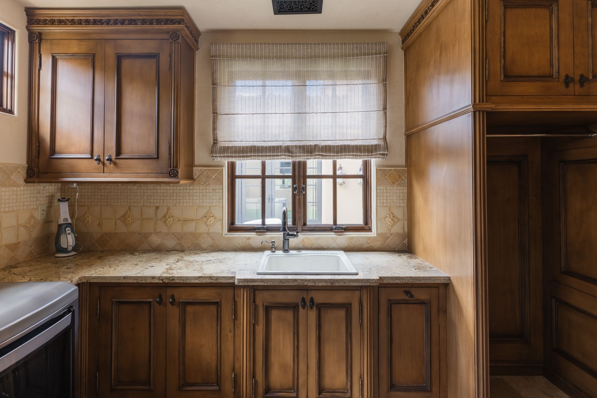 Kitchen with dark wood cabinets, granite countertop, window with Roman shade, and a farmhouse sink.