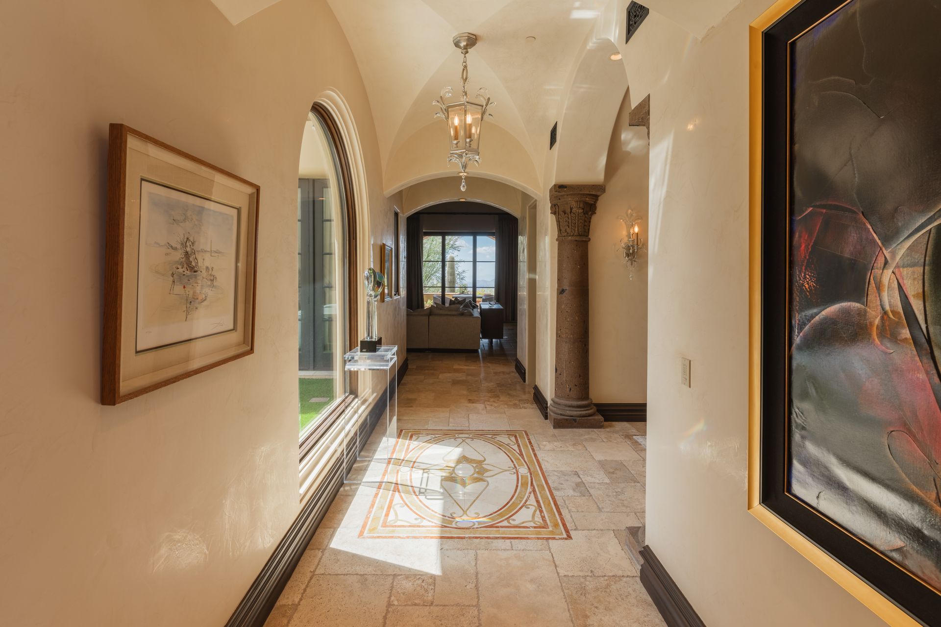 Long hallway with arched ceiling, light-colored walls and flooring, decorative art, and a view of the outside.