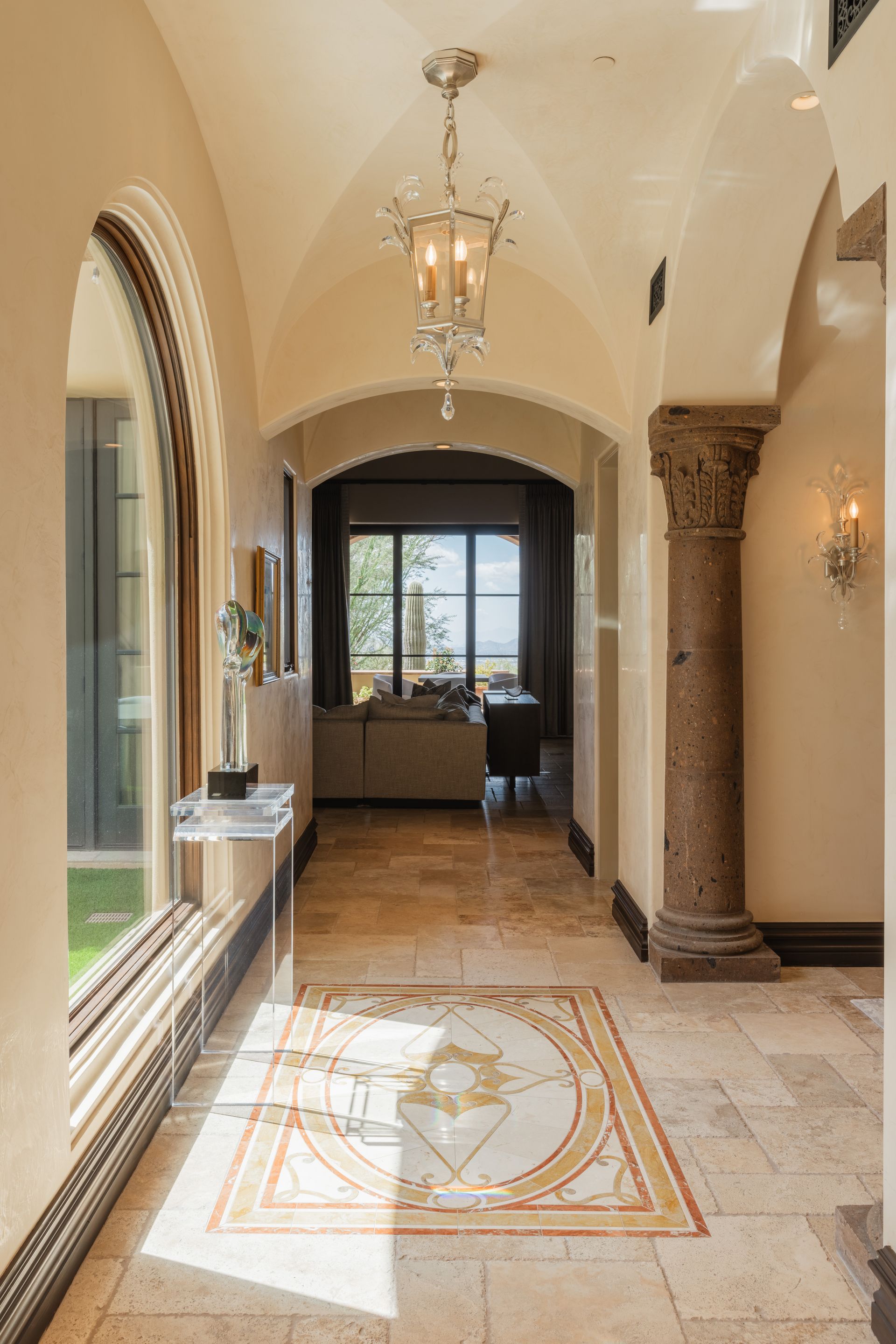 Elegant entryway with arched ceiling, patterned floor, and crystal chandelier.