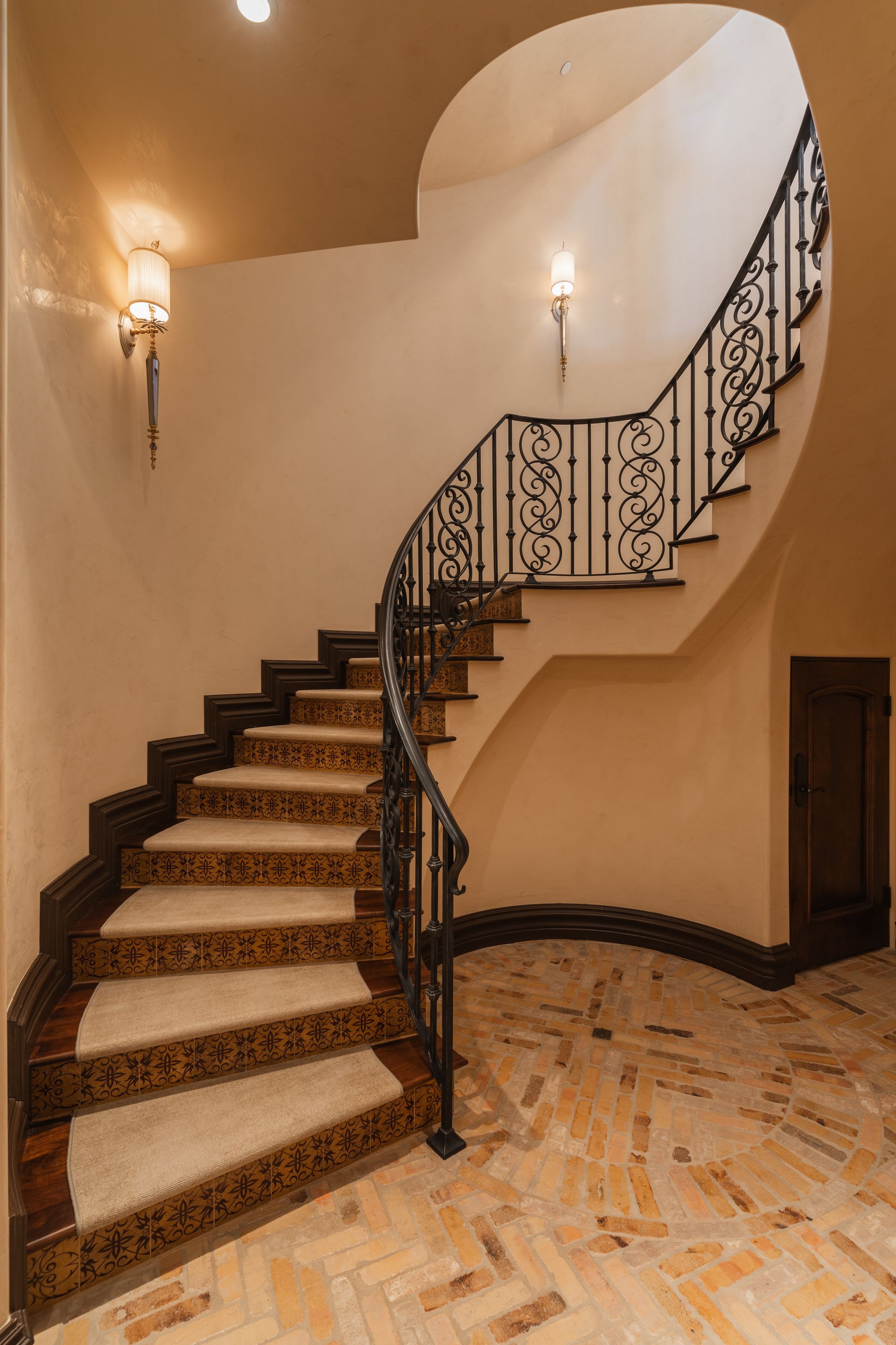 Elegant curved staircase with black iron railing, beige walls, and patterned tile flooring.