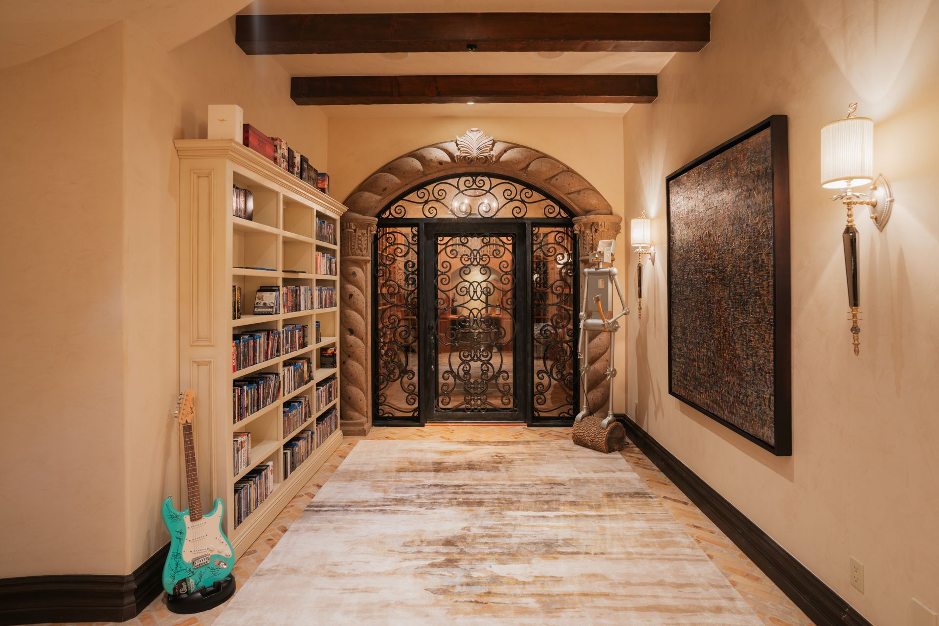 Hallway with arched doorway, bookcase, artwork, and guitar. Warm lighting, stone and wood details.