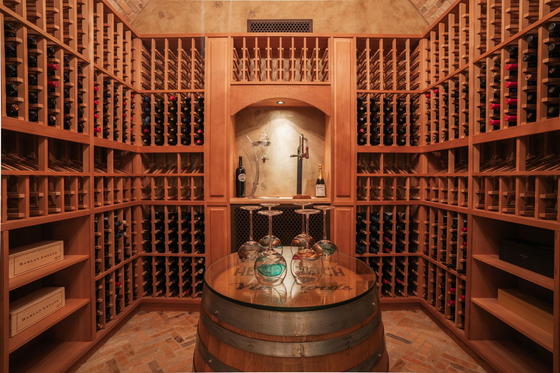 Wine cellar with wood racks holding bottles, center barrel table with glasses.