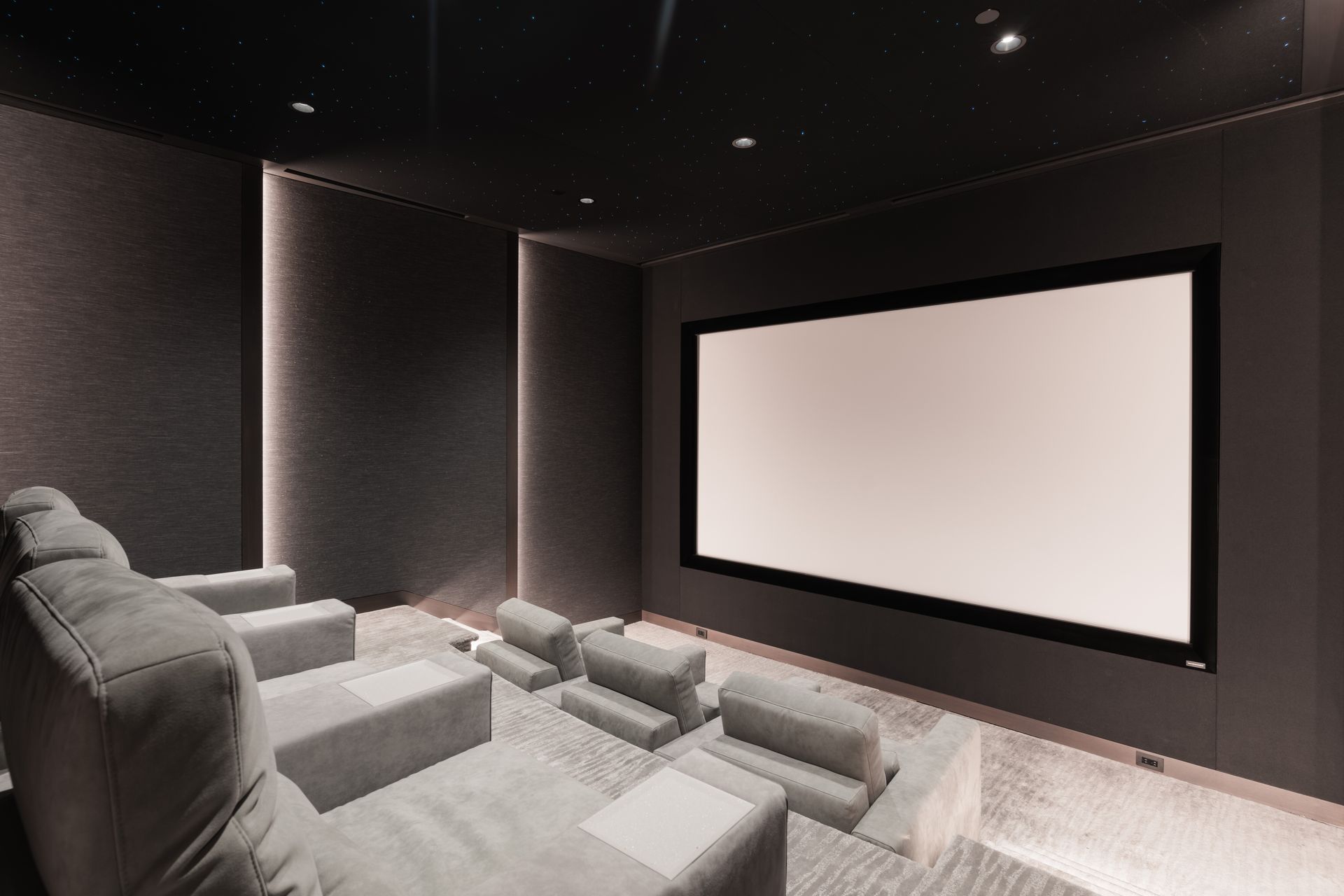 A modern home theater with gray seating, a large screen, and dark walls and ceiling.