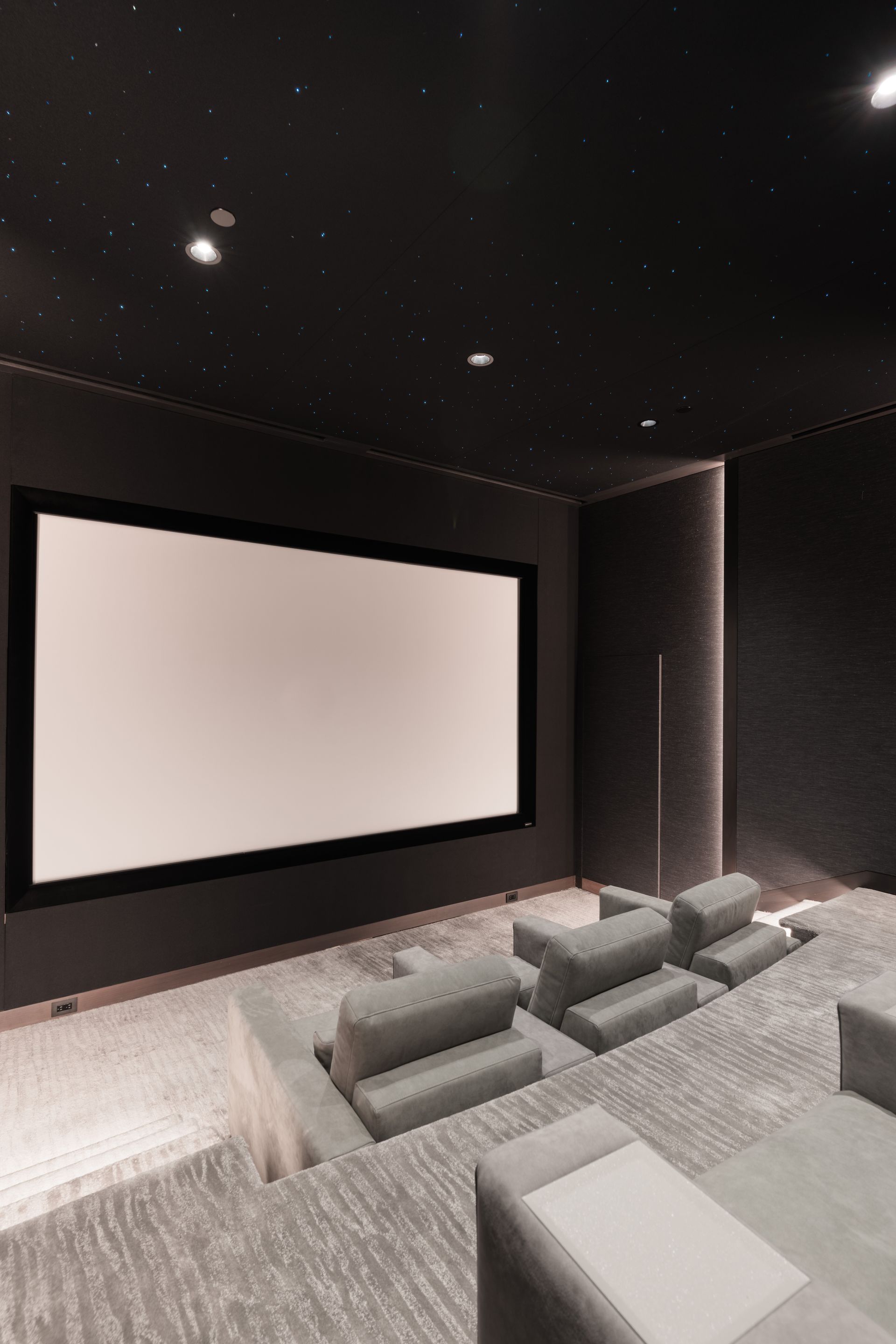 Home theater with tiered seating, large screen, and starry ceiling lights.