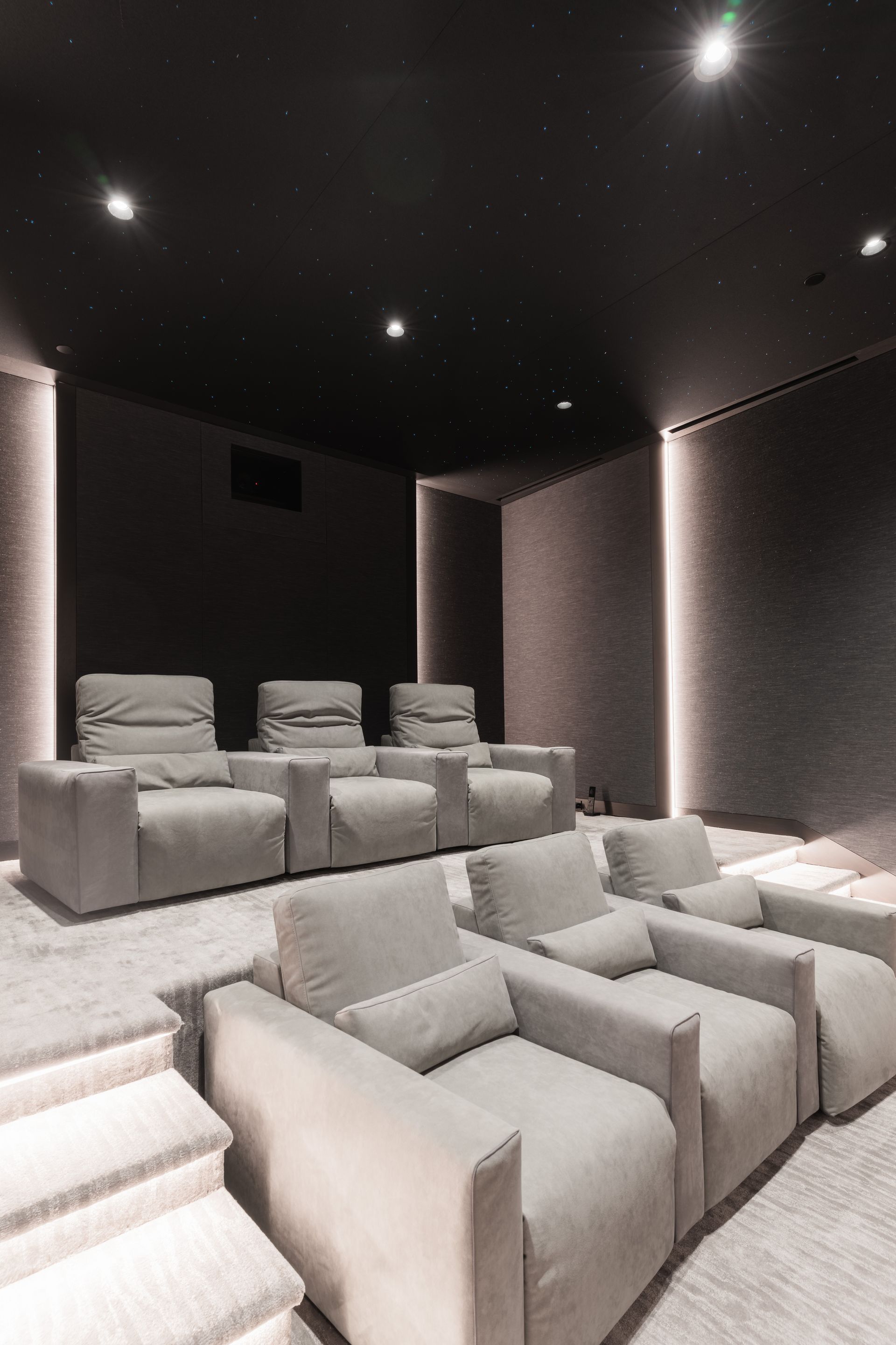 Cozy home theater with gray recliners on tiered levels, dark walls and starry ceiling.