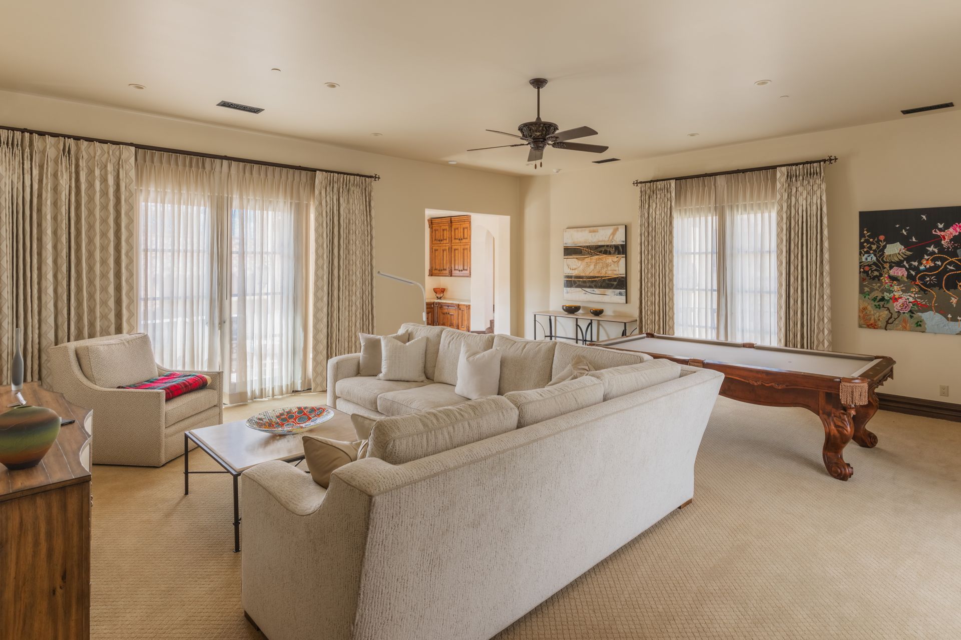 Spacious living room with sofa, chairs, pool table, windows, and neutral colors.