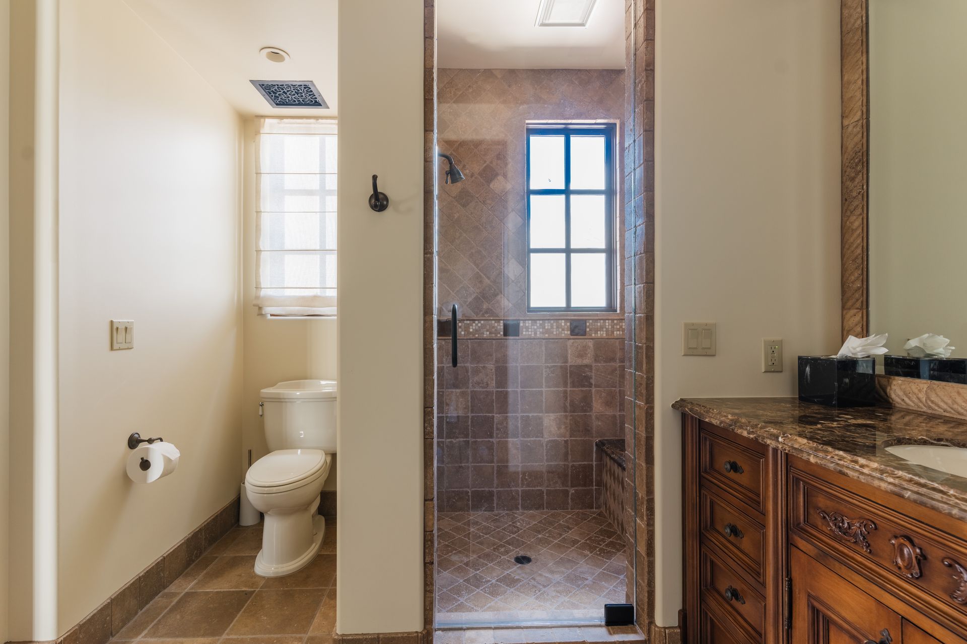 Bathroom with toilet, shower, and vanity. Tile floor, cream walls, dark wood vanity.