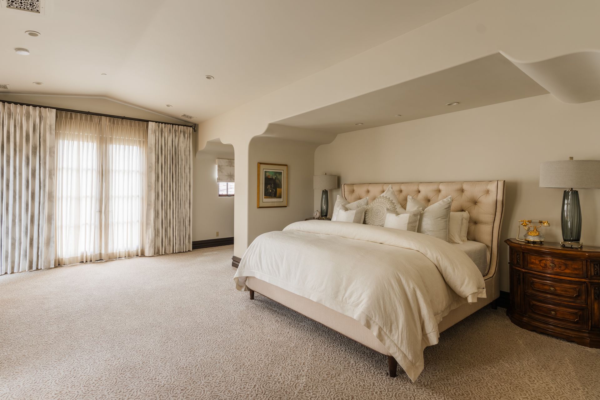 Spacious bedroom with large bed, curtains, carpet, and nightstand.