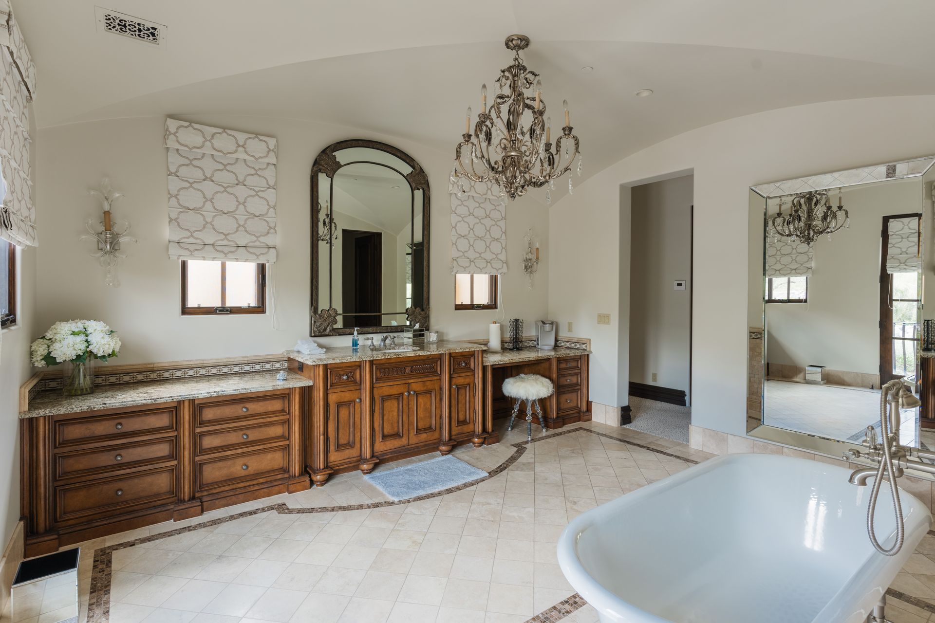 Luxurious bathroom with a chandelier, ornate wood cabinets, large mirrors, and a freestanding tub.