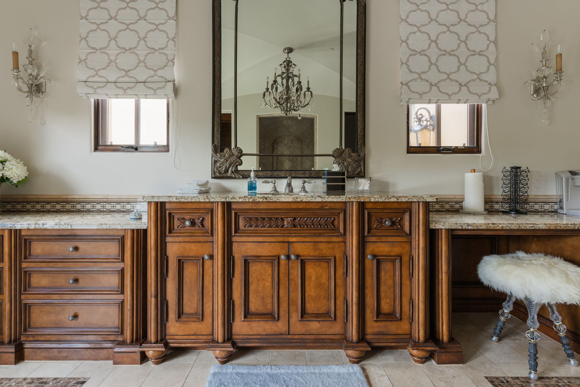 Bathroom with a large wooden vanity, ornate mirror, and decorative sconces. Light-colored walls and countertops.