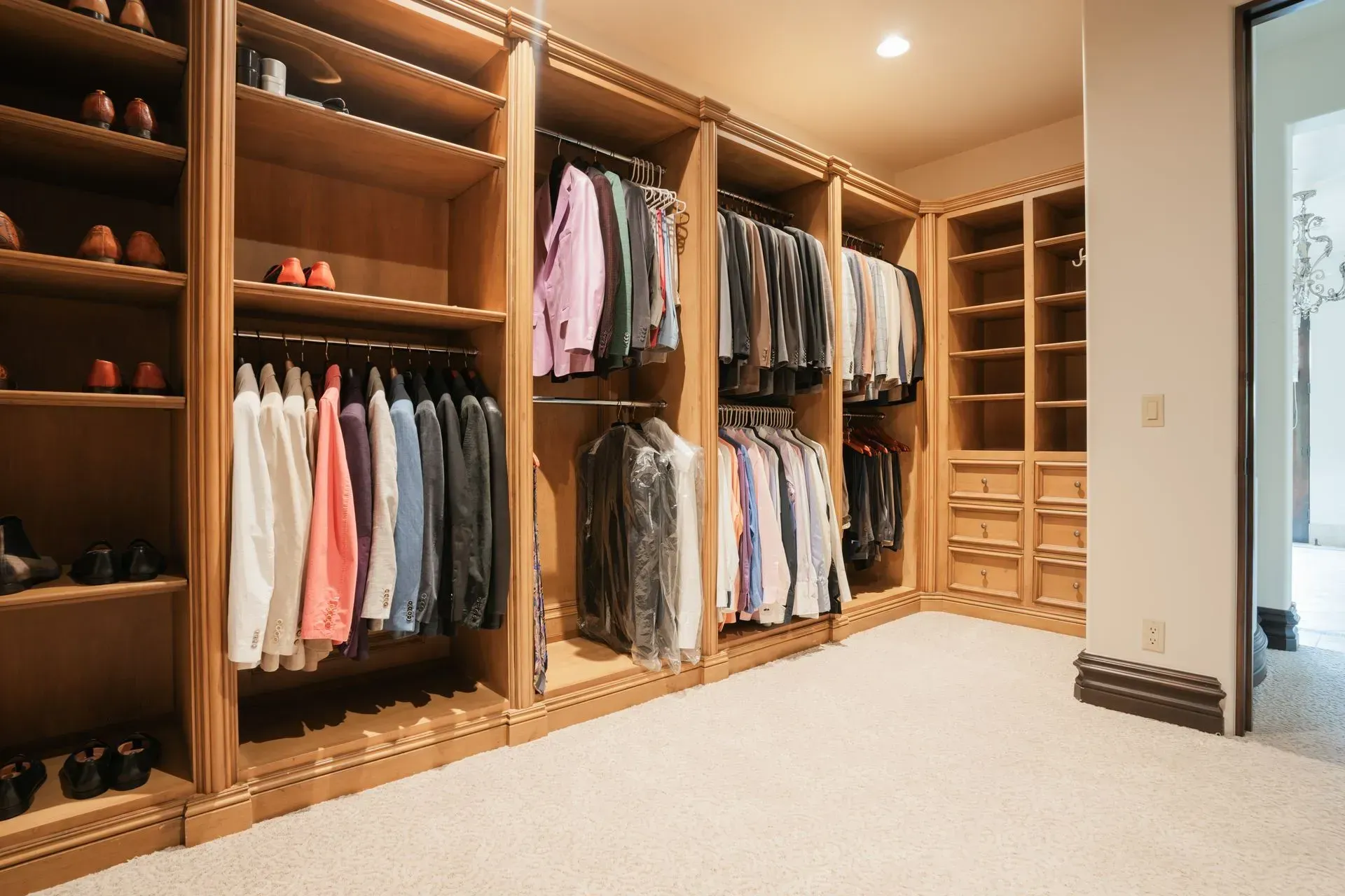 Walk-in closet with light wood shelving and hanging clothes on racks. Cream carpet.
