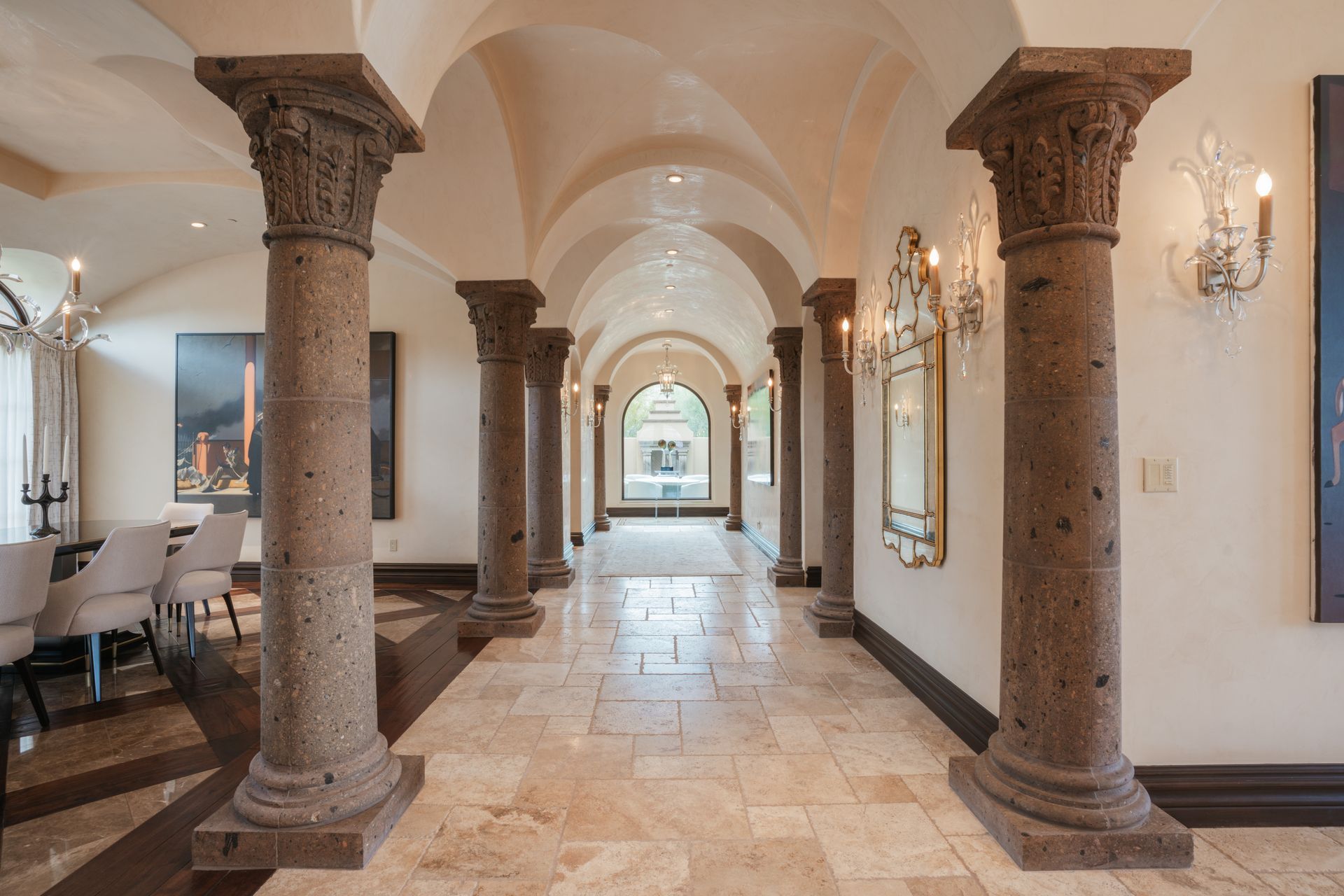 Stone columns line a hallway with a vaulted ceiling. Dining room on the left, glass doors at the end.