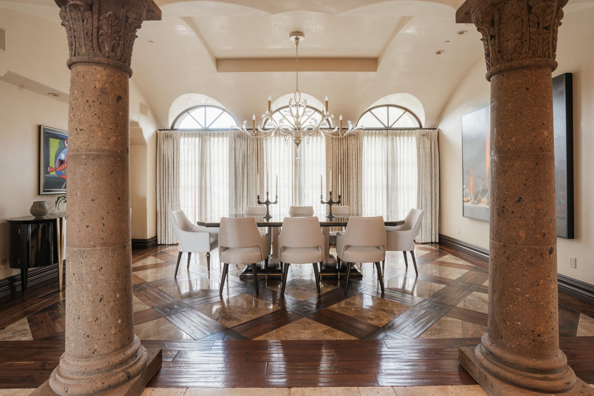 Elegant dining room with arched windows, chandelier, long table, and decorative flooring.