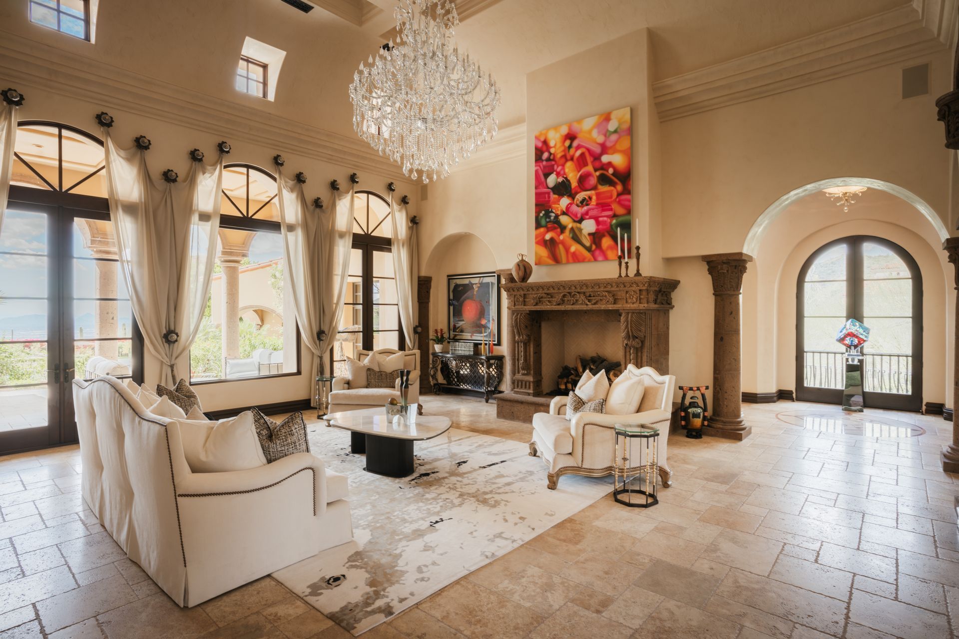 Elegant living room with white furniture, chandelier, fireplace, and large colorful painting.