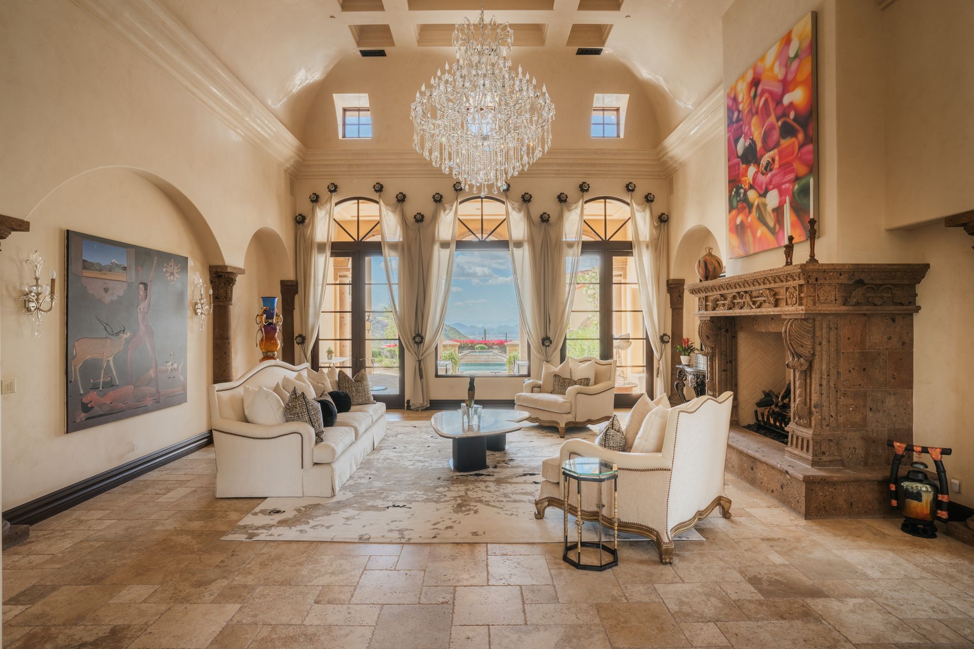 Luxurious living room with ornate fireplace, large windows, chandelier, and white furniture.